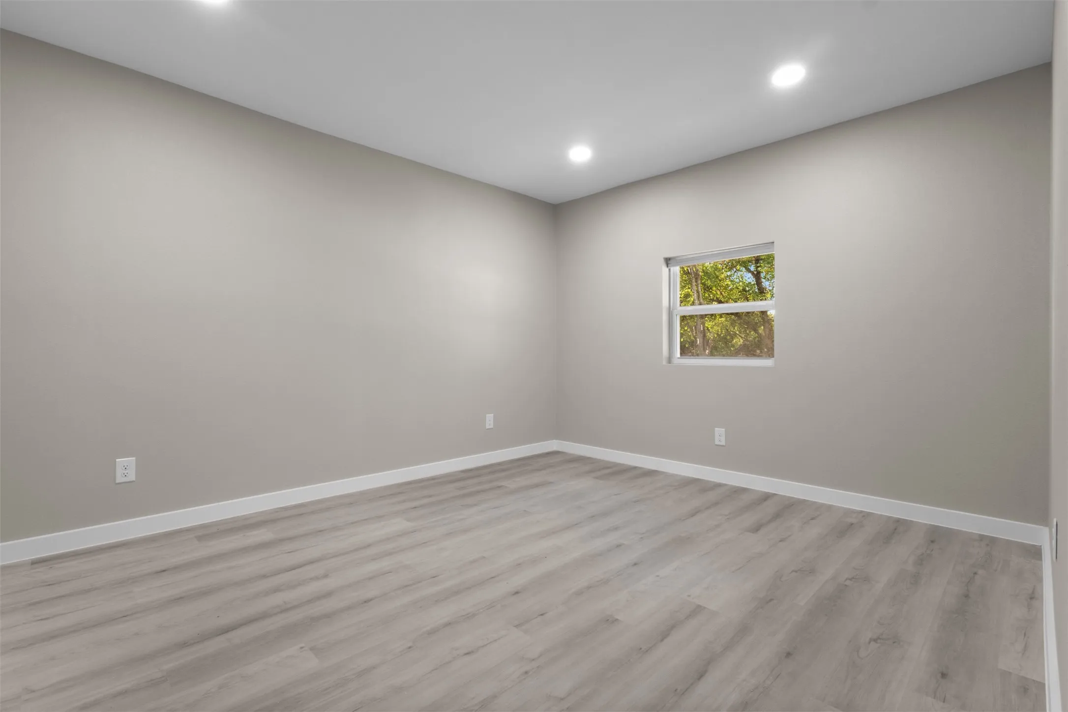 Recessed ceiling lighting, light gray wall color, a single window, and wood-finish flooring