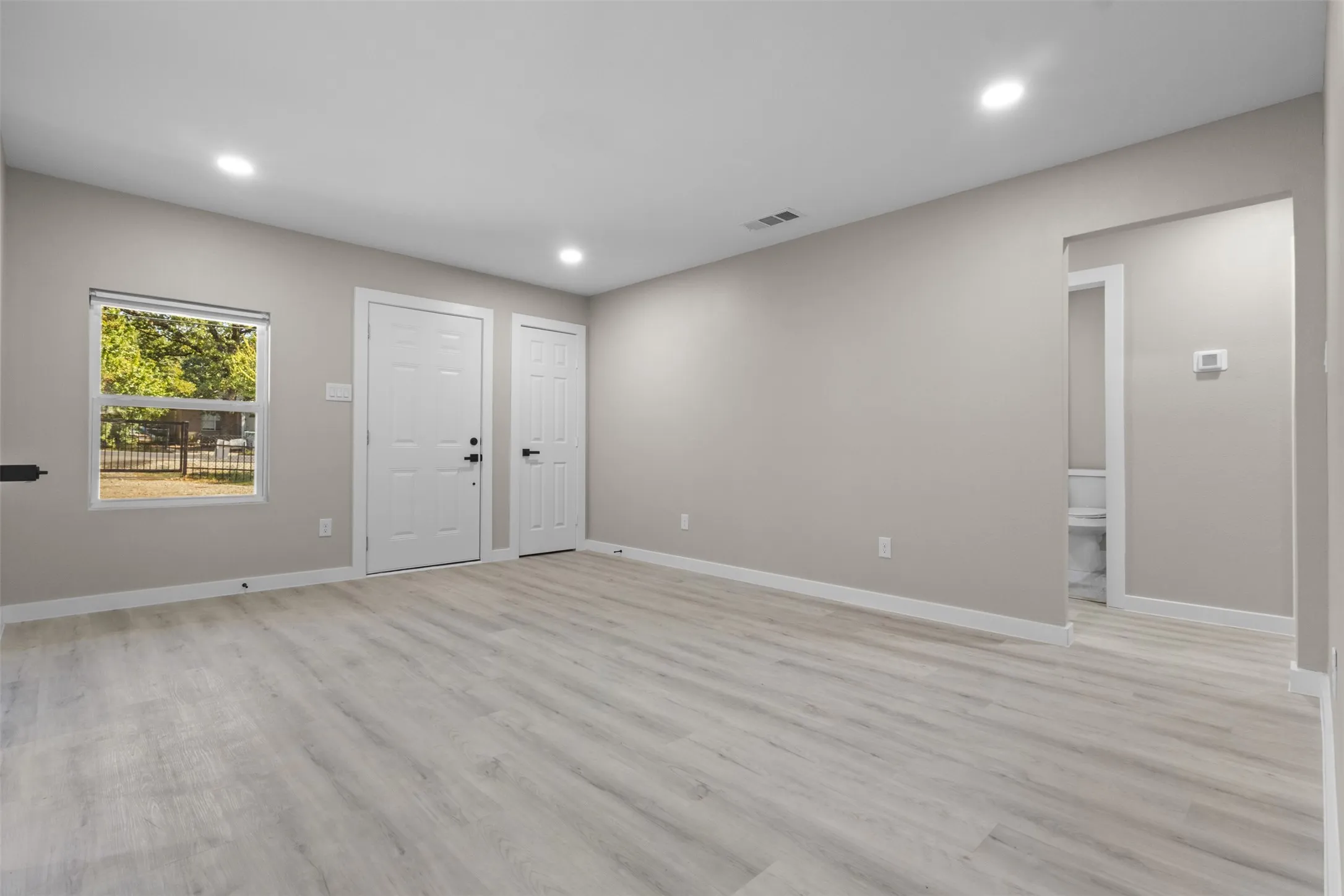 Recessed lighting, light wood-finish flooring, neutral wall tones, white trim, and a window with outdoor scenery