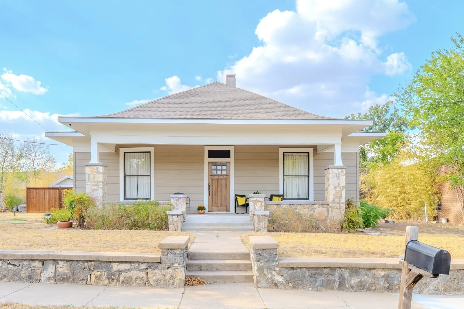 Craftsman-style home featuring a covered front porch, stone-clad columns, and a wood-paneled entry door
