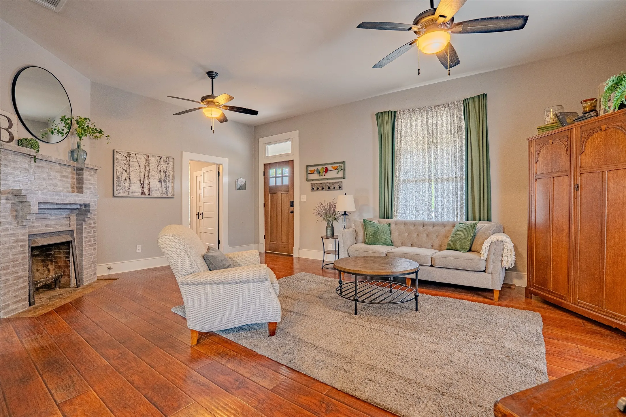 Laminate flooring throughout, brick fireplace with mantel, two ceiling fans with integrated lighting, and a wood entry door with glass panels
