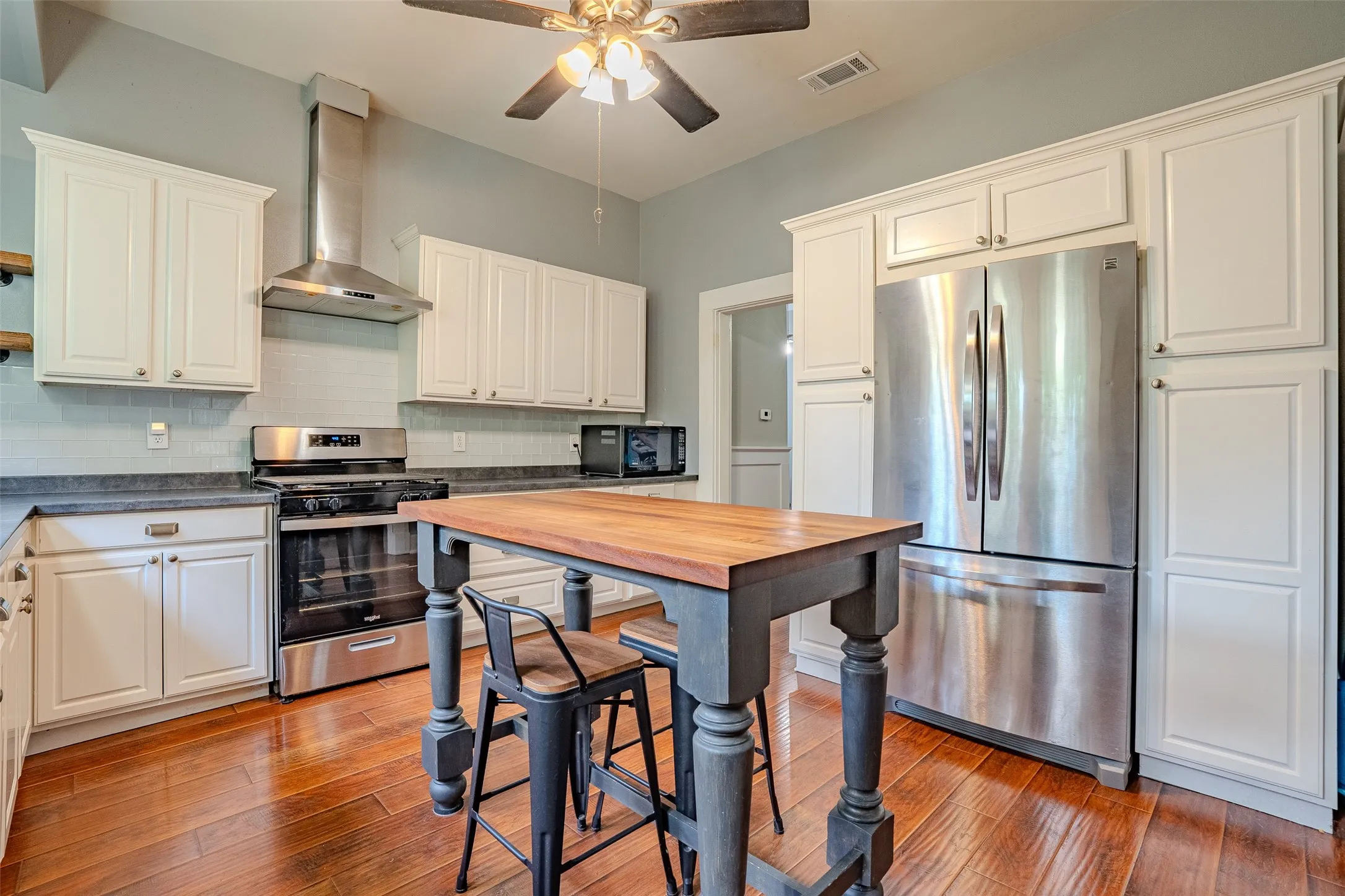 Stainless steel appliances, white cabinetry, laminate flooring, light-colored subway tile backsplash, and dark countertops