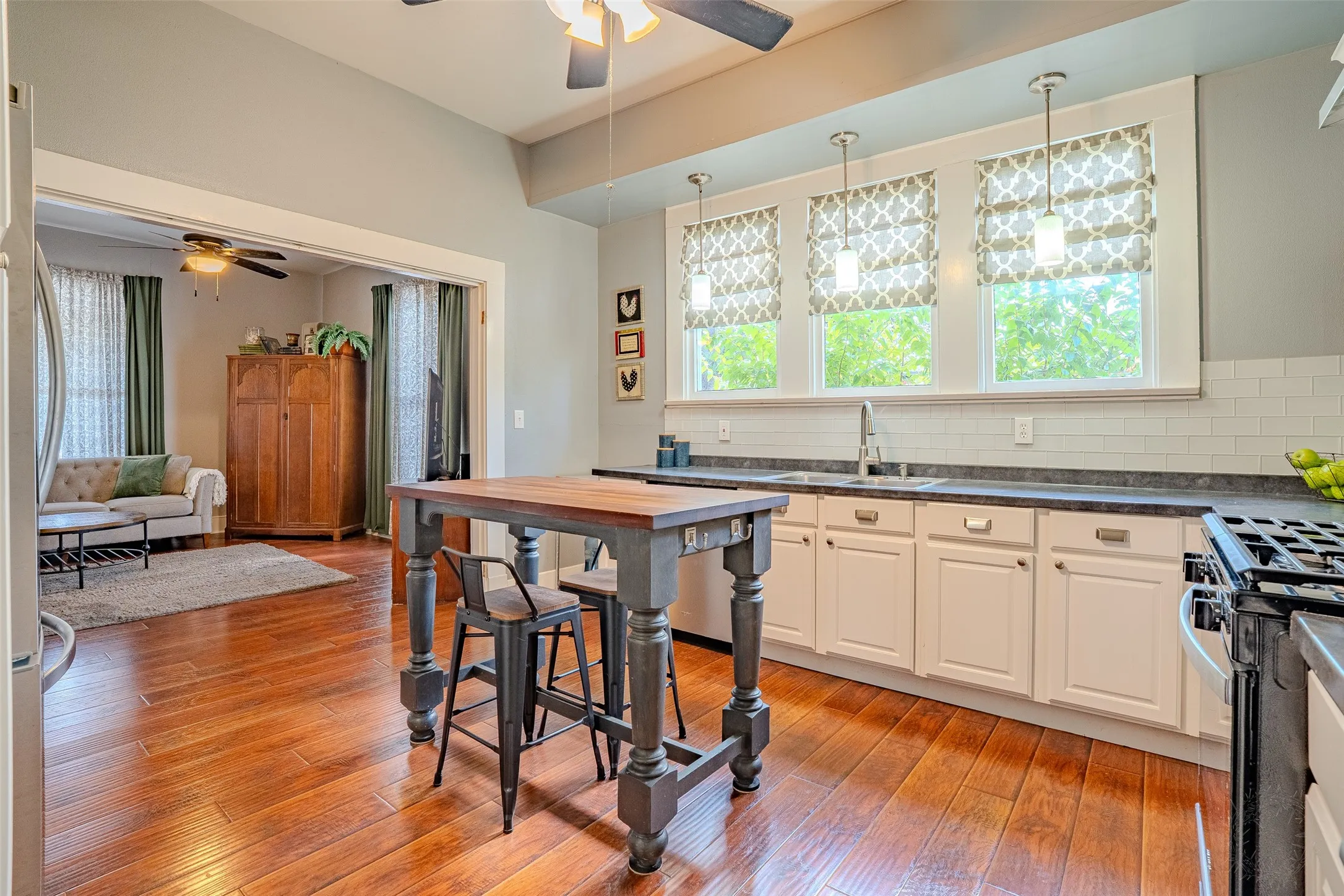 Laminate flooring, white shaker-style cabinetry, subway tile backsplash, recessed sink, and pendant lighting