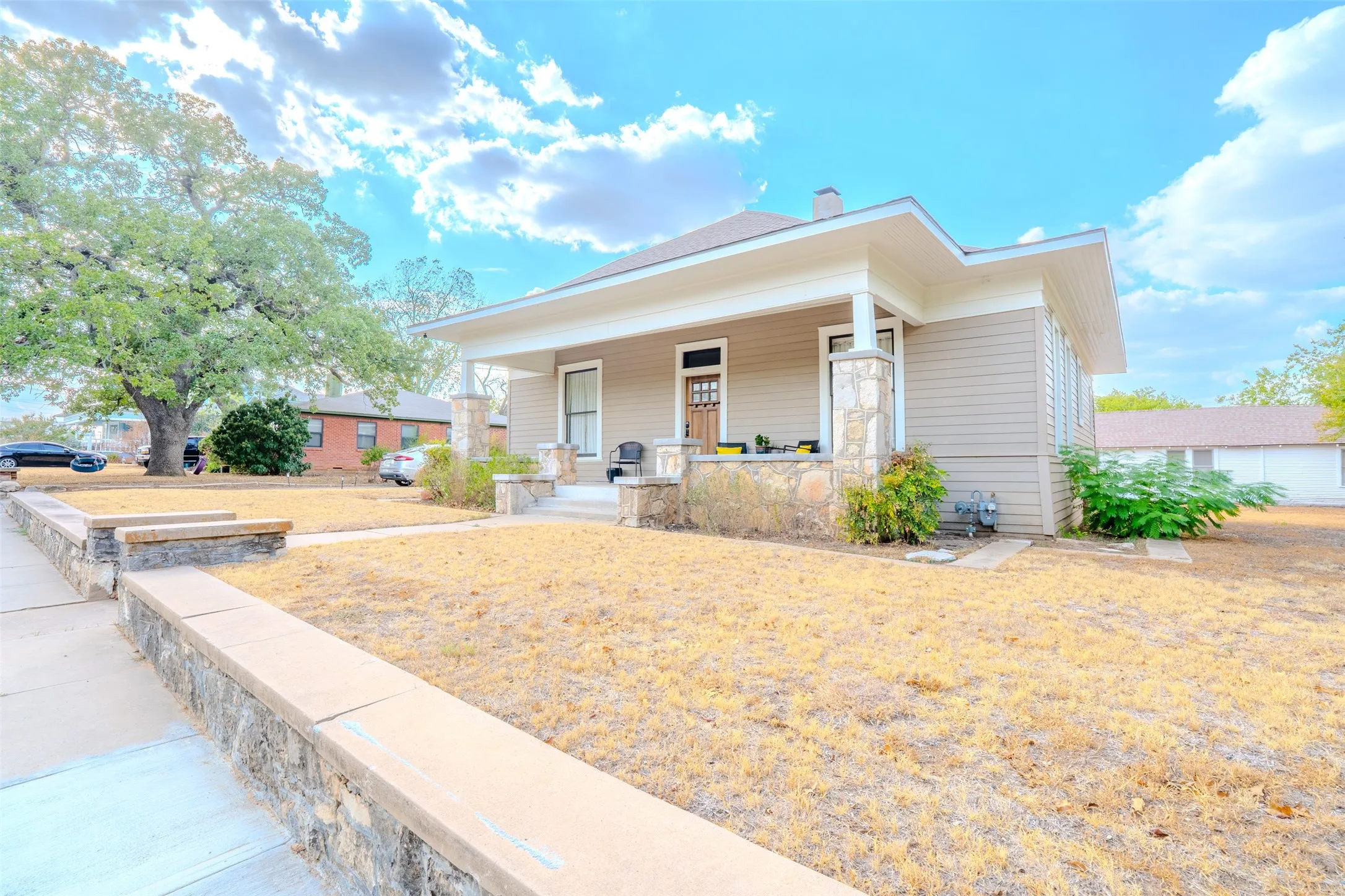 Craftsman-style home featuring a covered front porch with stone and wood columns, horizontal siding, and a prominent front door with decorative glass inserts