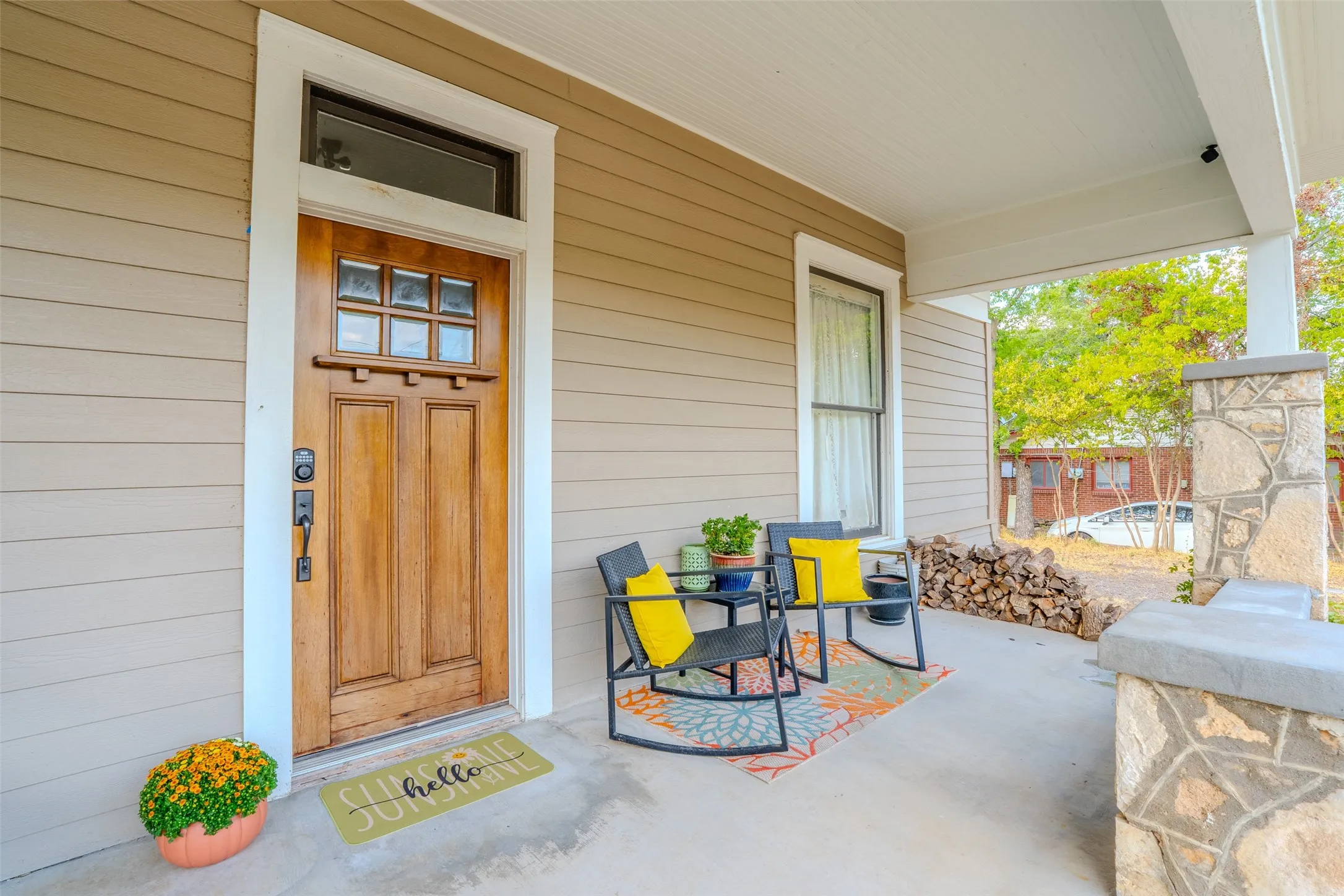 Covered front porch featuring a wood-panel door with transom window, horizontal siding, and a stone-clad column