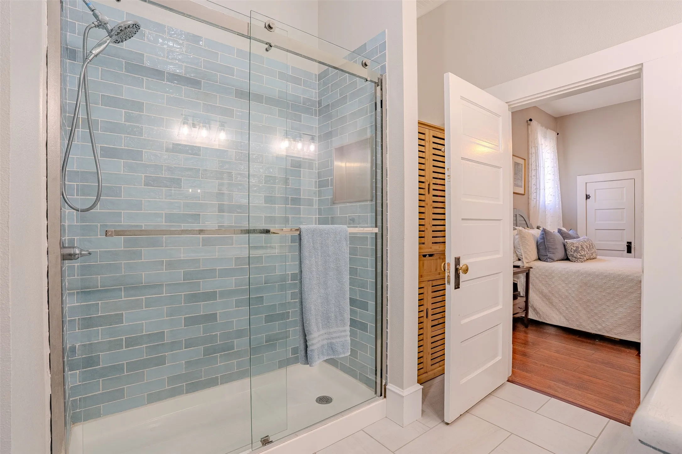 Glass-enclosed shower with blue subway tile surround and a handheld showerhead