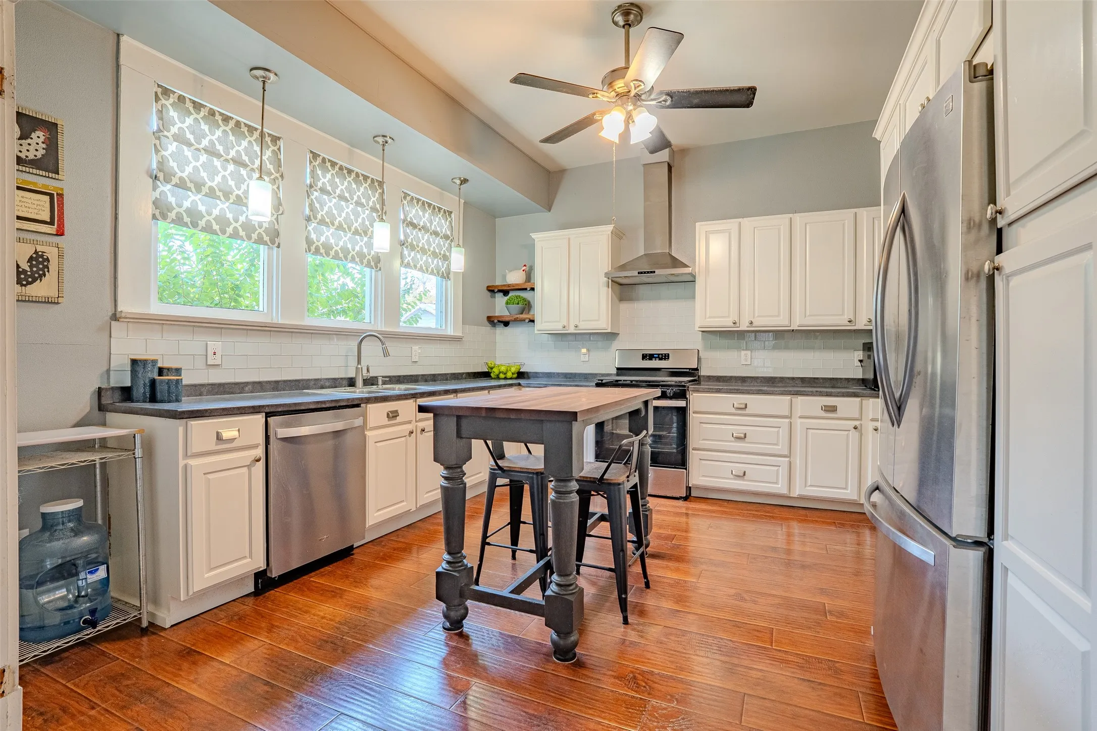 Kitchen featuring laminate flooring, white cabinetry, dark countertops, stainless steel appliances, and a tile backsplash