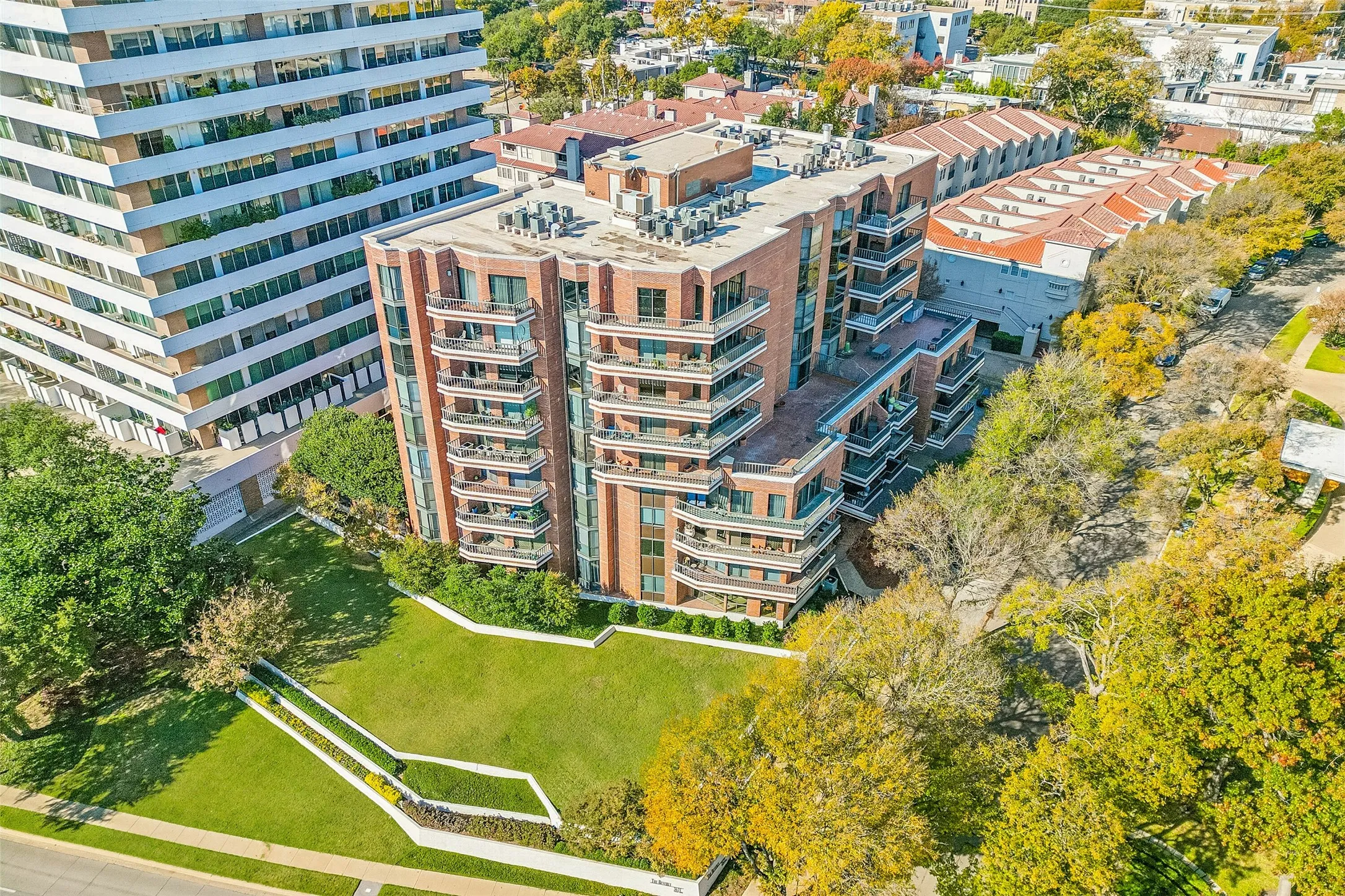 Multi-story building featuring brick and glass construction, individual balconies, and a manicured green space