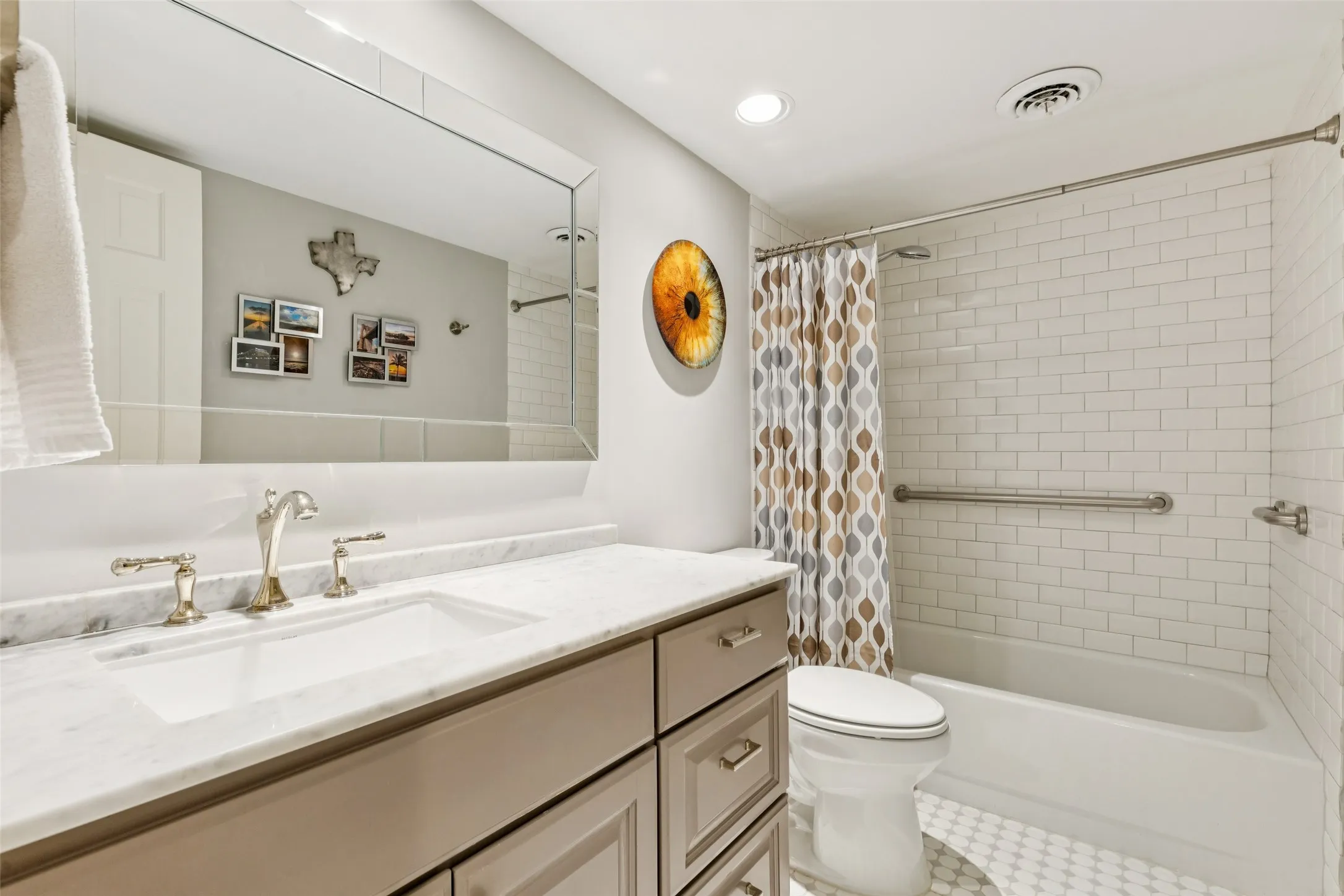 Vanity with an undermount sink and a light-colored countertop, polished nickel-finish fixtures, a large rectangular mirror, a subway-tiled bath, and white hexagon-tile flooring