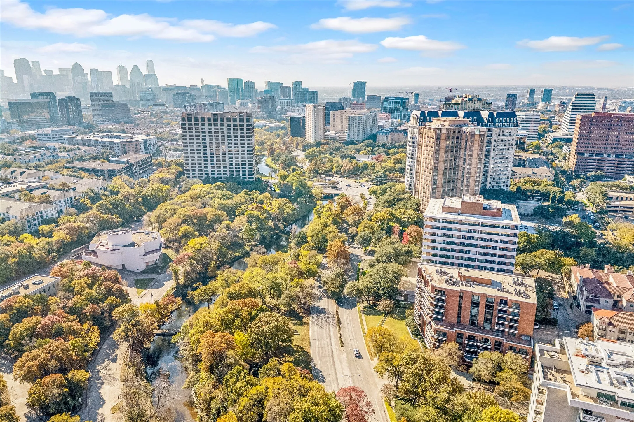 Expansive urban landscape featuring a prominent city skyline, numerous high-rise buildings, extensive tree canopy, and visible roadways