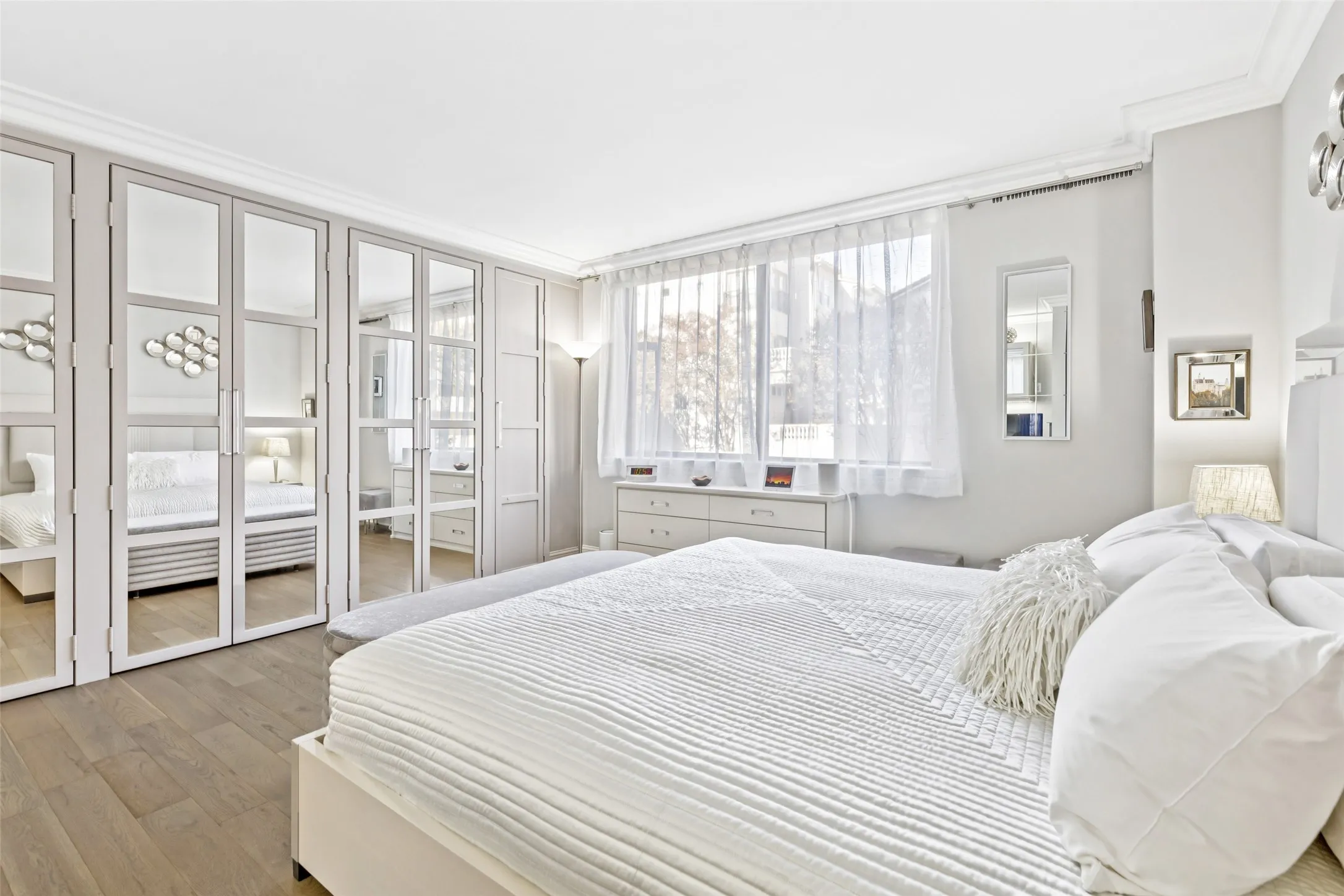 Mirrored wardrobe doors, built-in dresser, crown molding, and wood-finish flooring