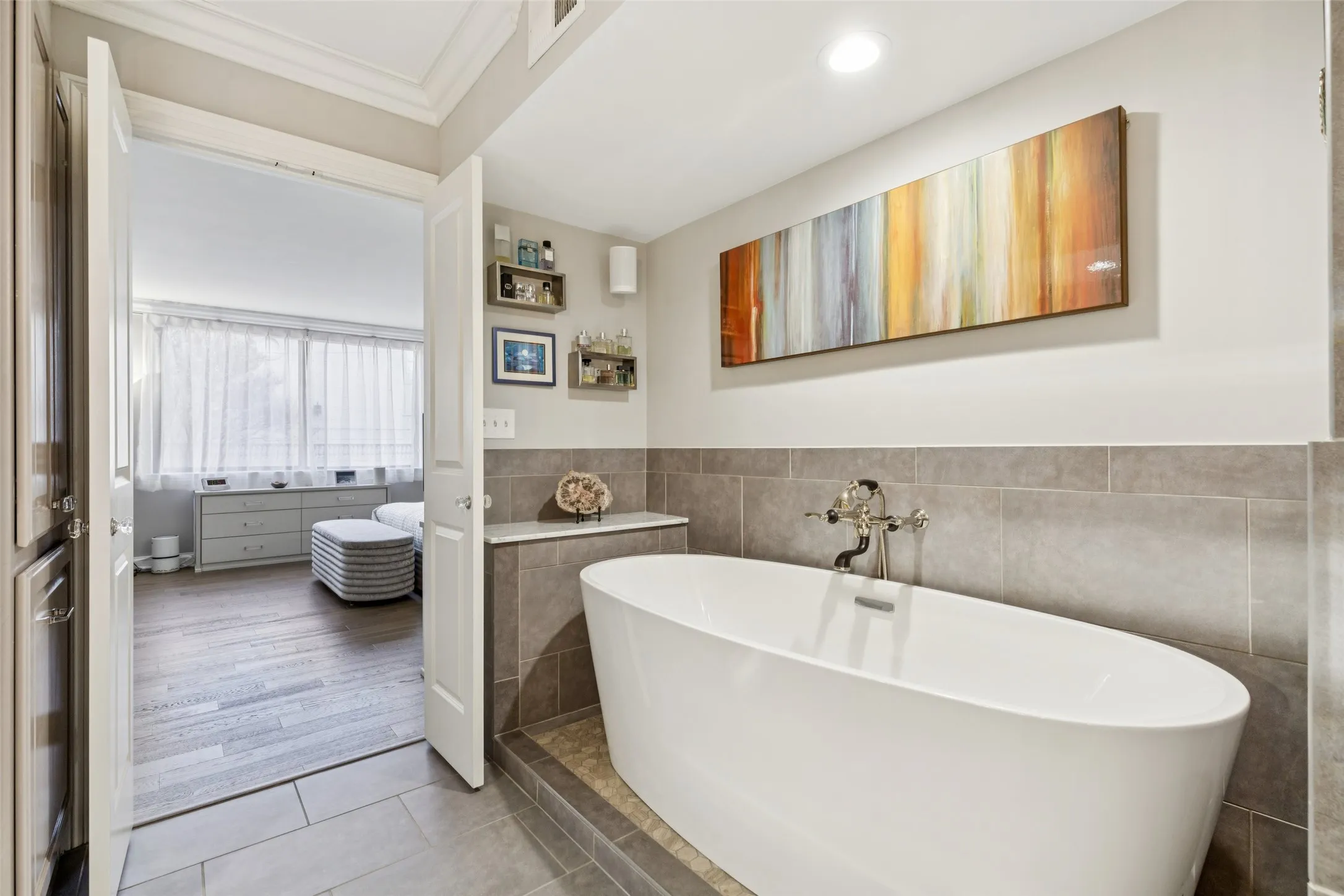 Freestanding soaking tub with floor-mounted faucet, tile surround, recessed lighting, and wood-finish flooring