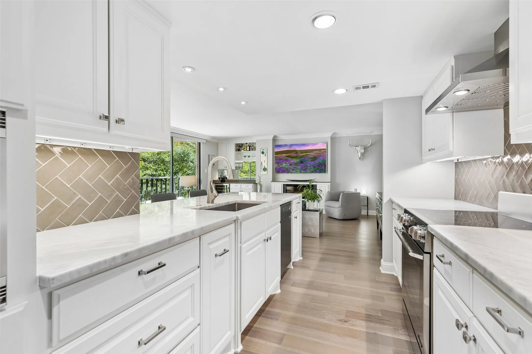White cabinetry, light-toned wood-finish flooring, recessed lighting, and stainless steel appliances