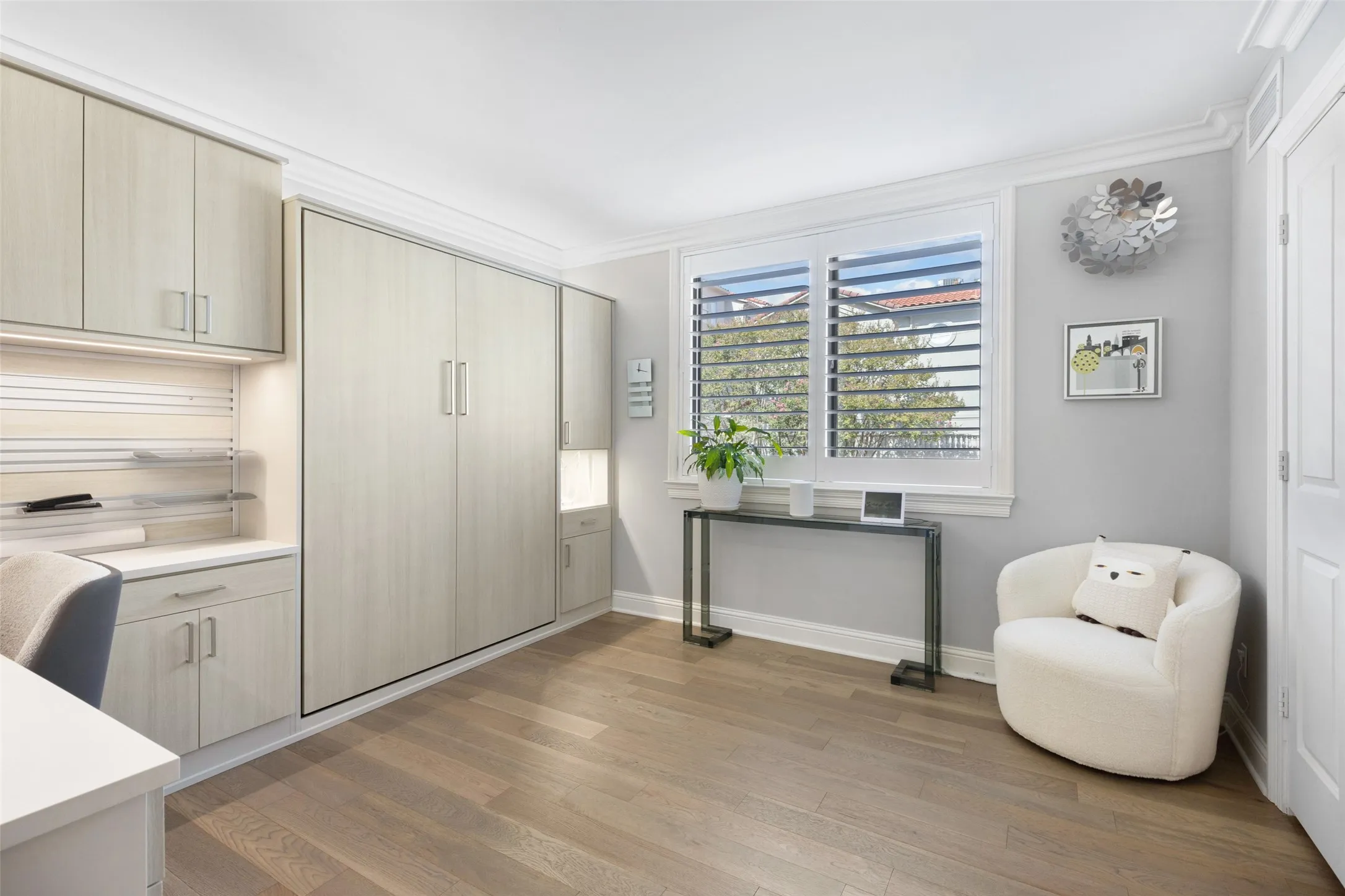 Integrated built-in cabinetry with under-cabinet lighting, wood-finish flooring, a built-in wall bed, crown molding, and plantation shutters