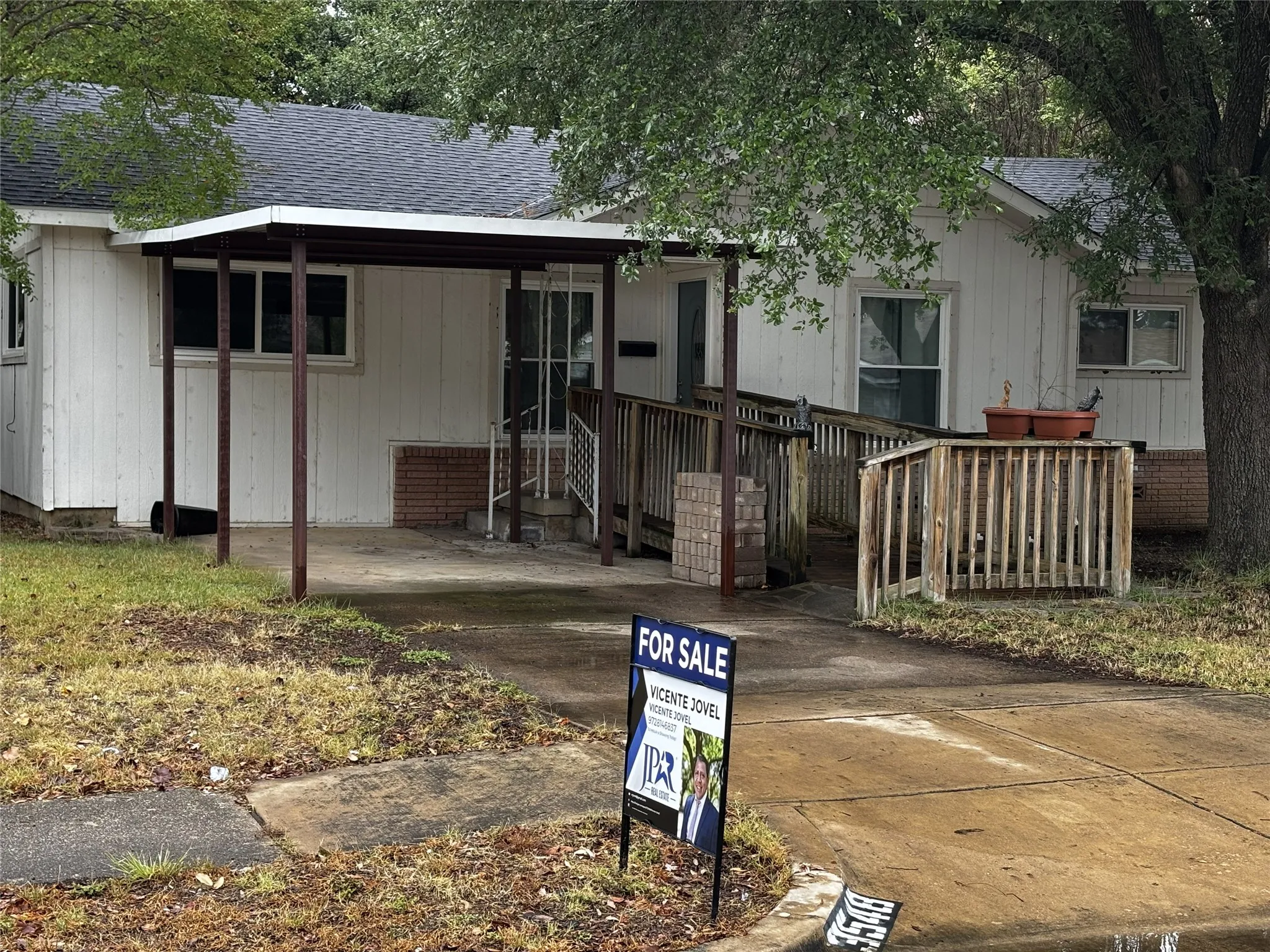 White siding exterior with a dark shingle roof, covered carport, and a wooden accessibility ramp