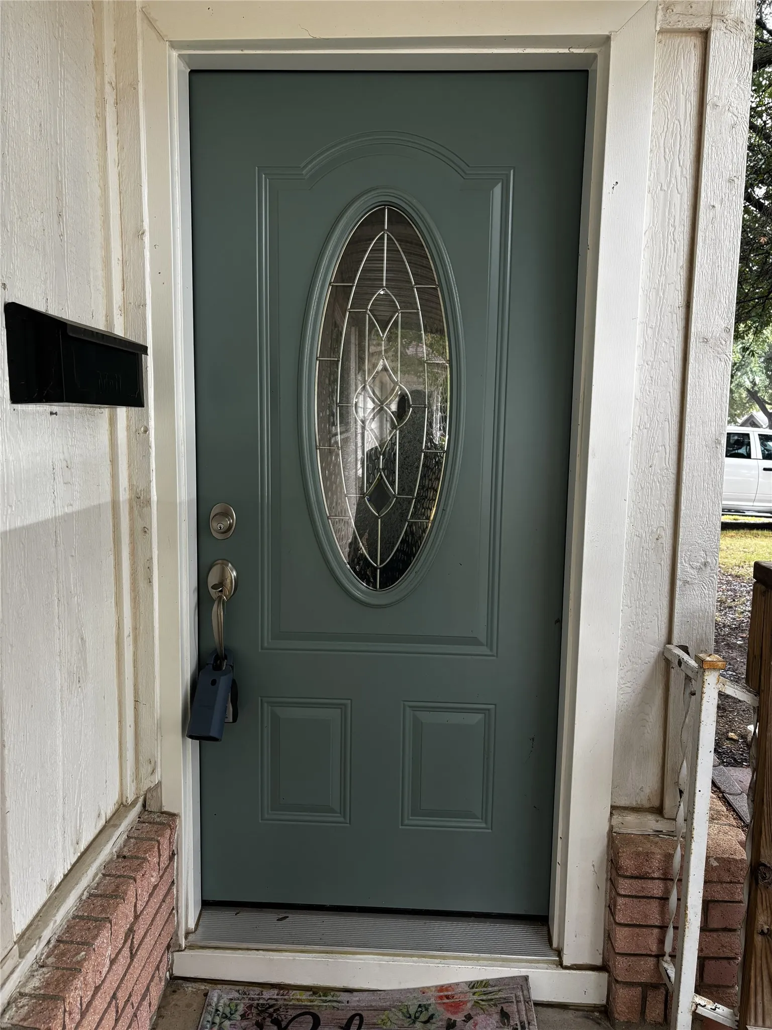 Paneled entry door with decorative oval glass insert, brick foundation details, and white trim