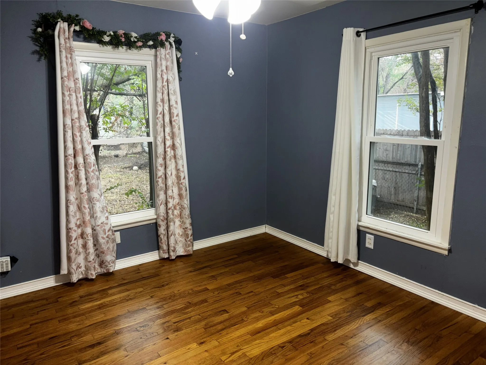Hardwood flooring with a glossy finish, two white-framed windows, and a ceiling-mounted light fixture