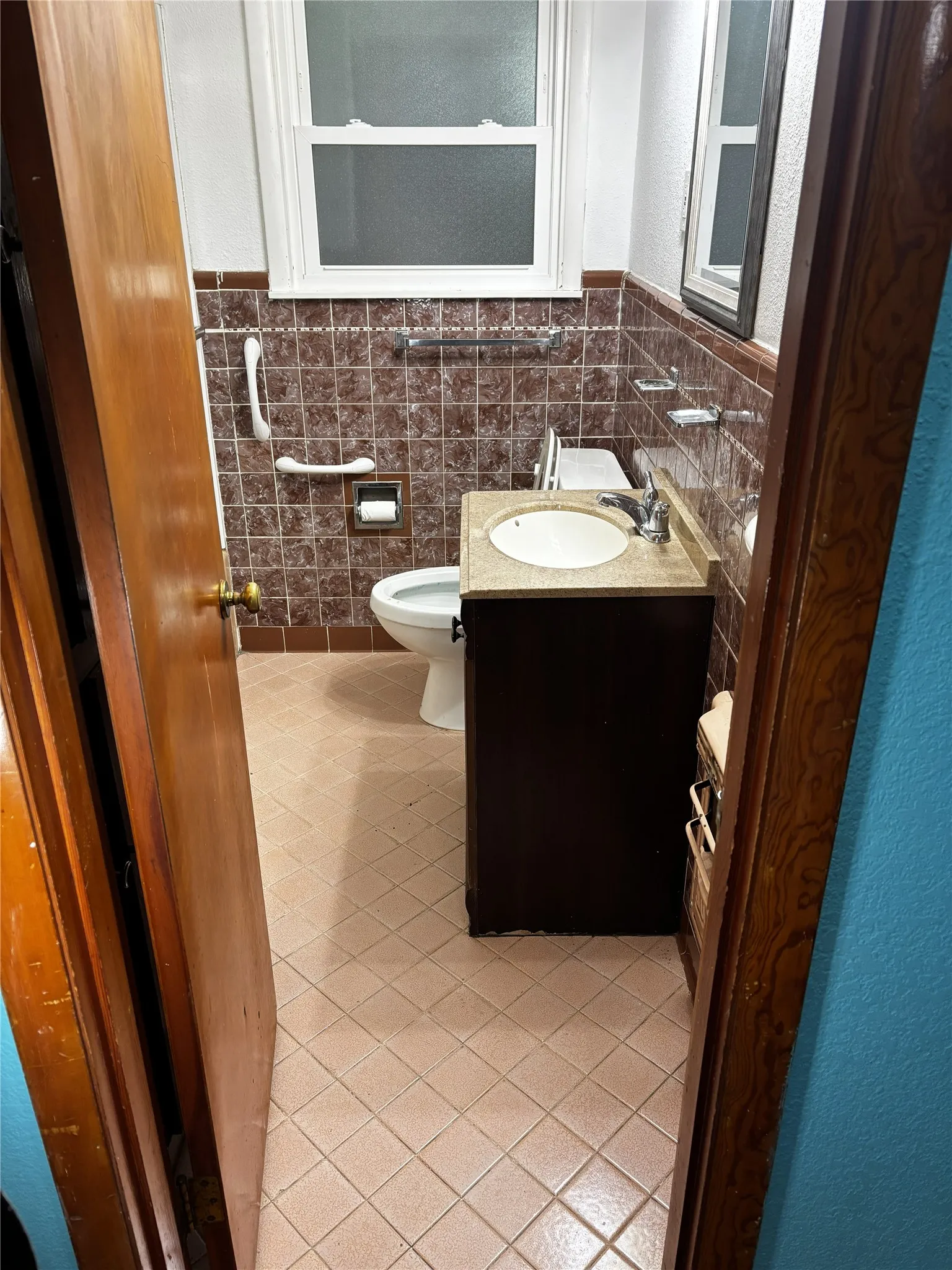 Bathroom featuring tiled walls, a single window, a vanity with an integrated sink, and light-toned floor tiles
