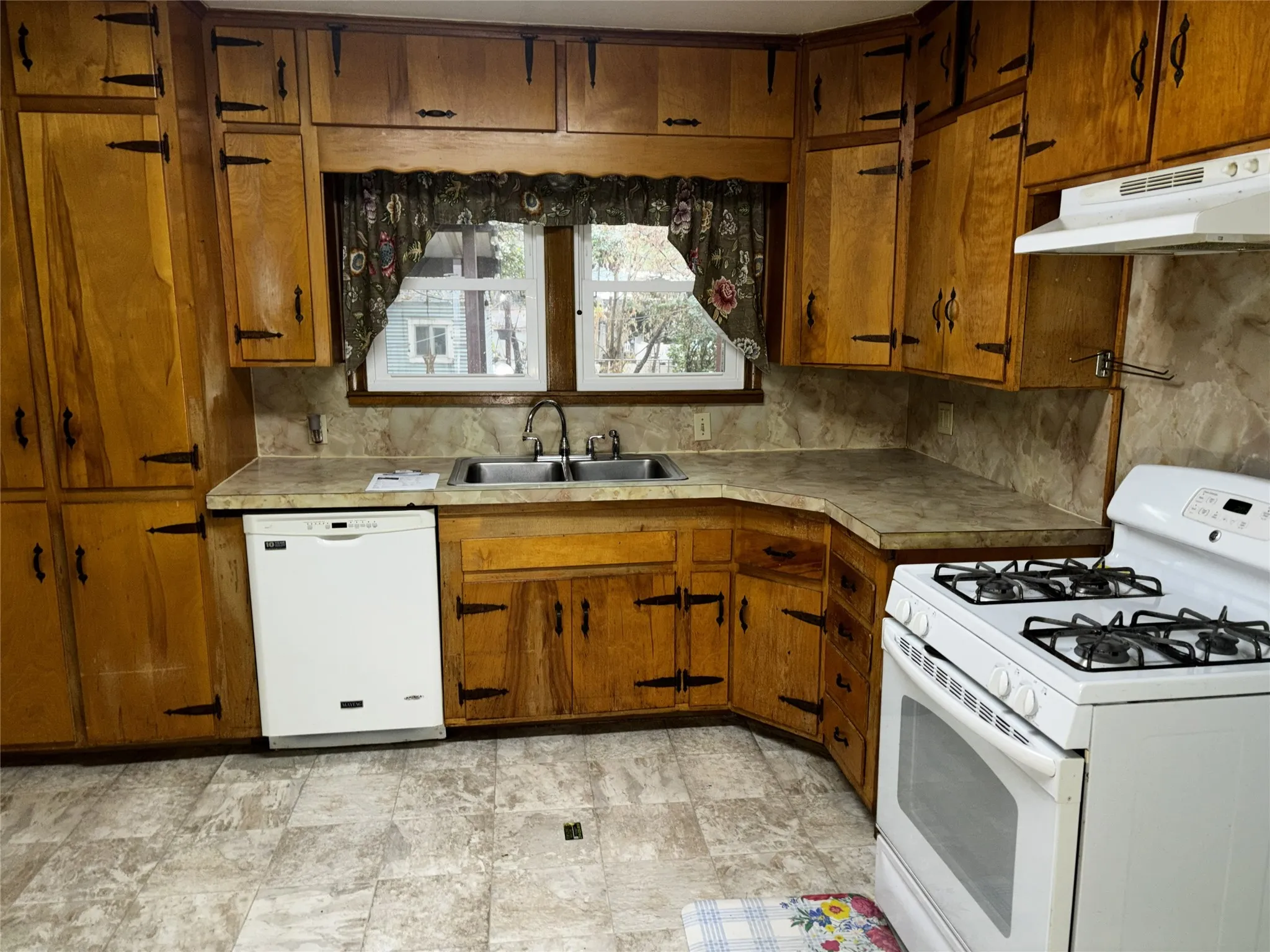 Wood-finish cabinetry with decorative hardware, solid surface countertops, and an integrated double basin sink
