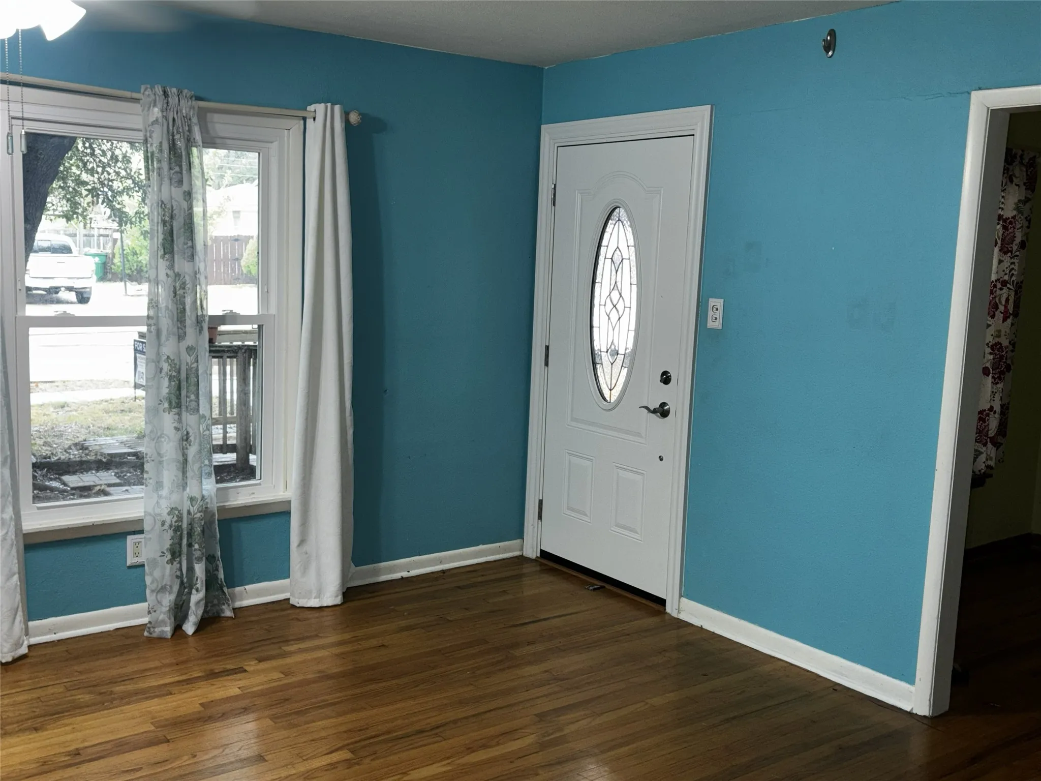 Hardwood flooring with a white trim baseboard, white door with an oval glass insert, and a double window
