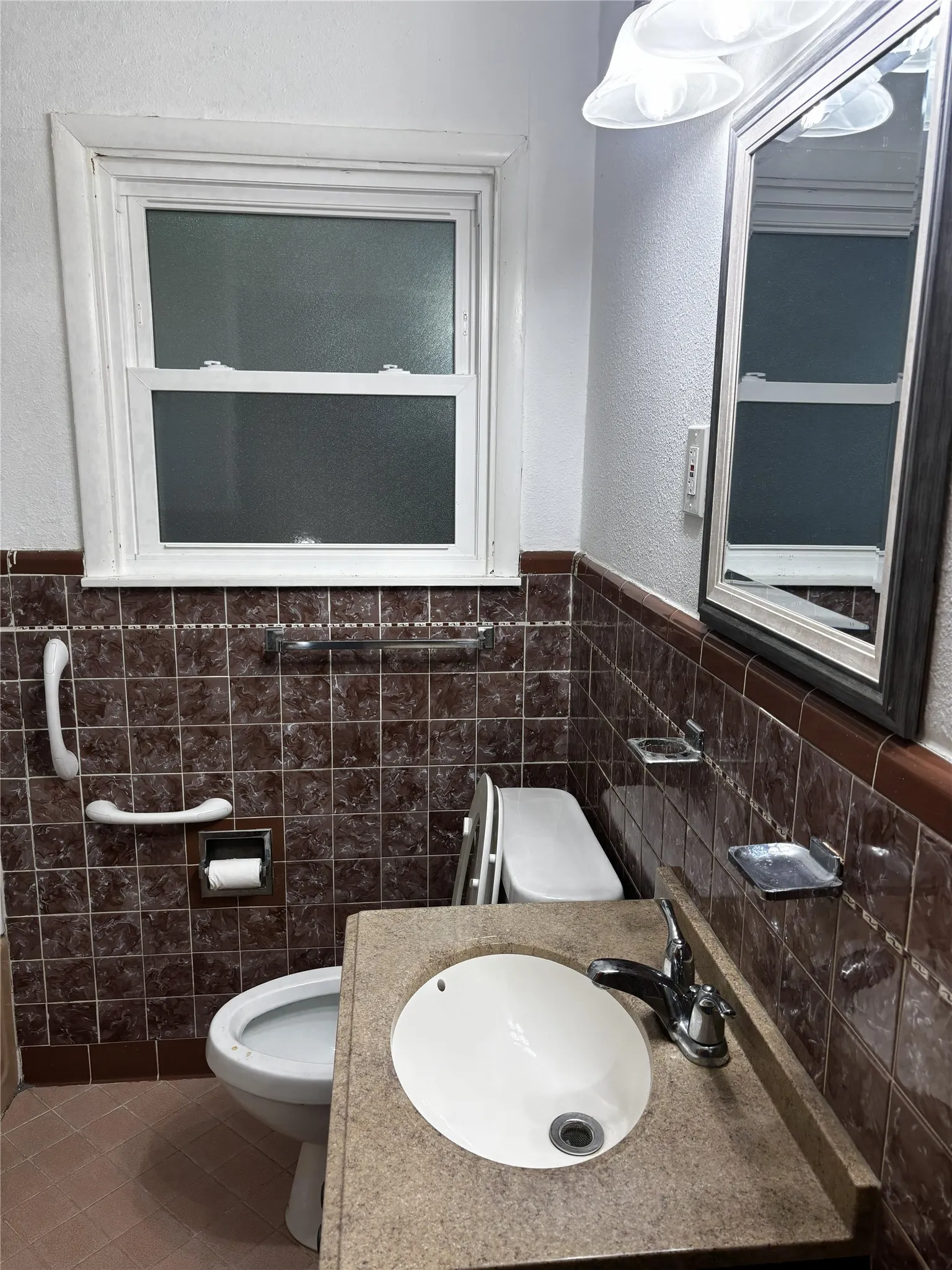 Single-pane window, tile wainscoting, built-in vanity with integrated sink, chrome faucet, and wall-mounted mirror