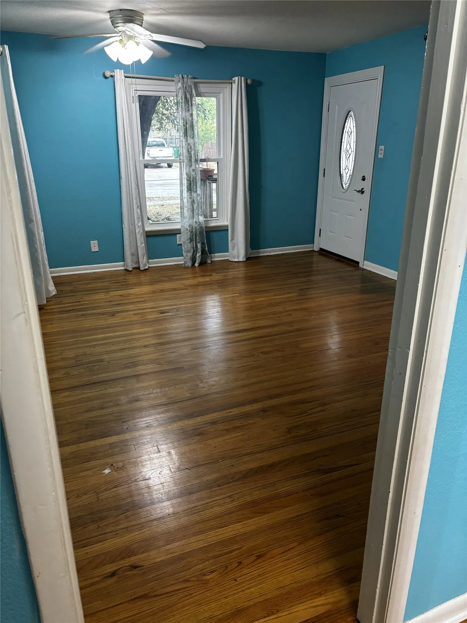 Warm wood-finish flooring, a ceiling fan with integrated lighting, and a white entry door with an oval glass insert