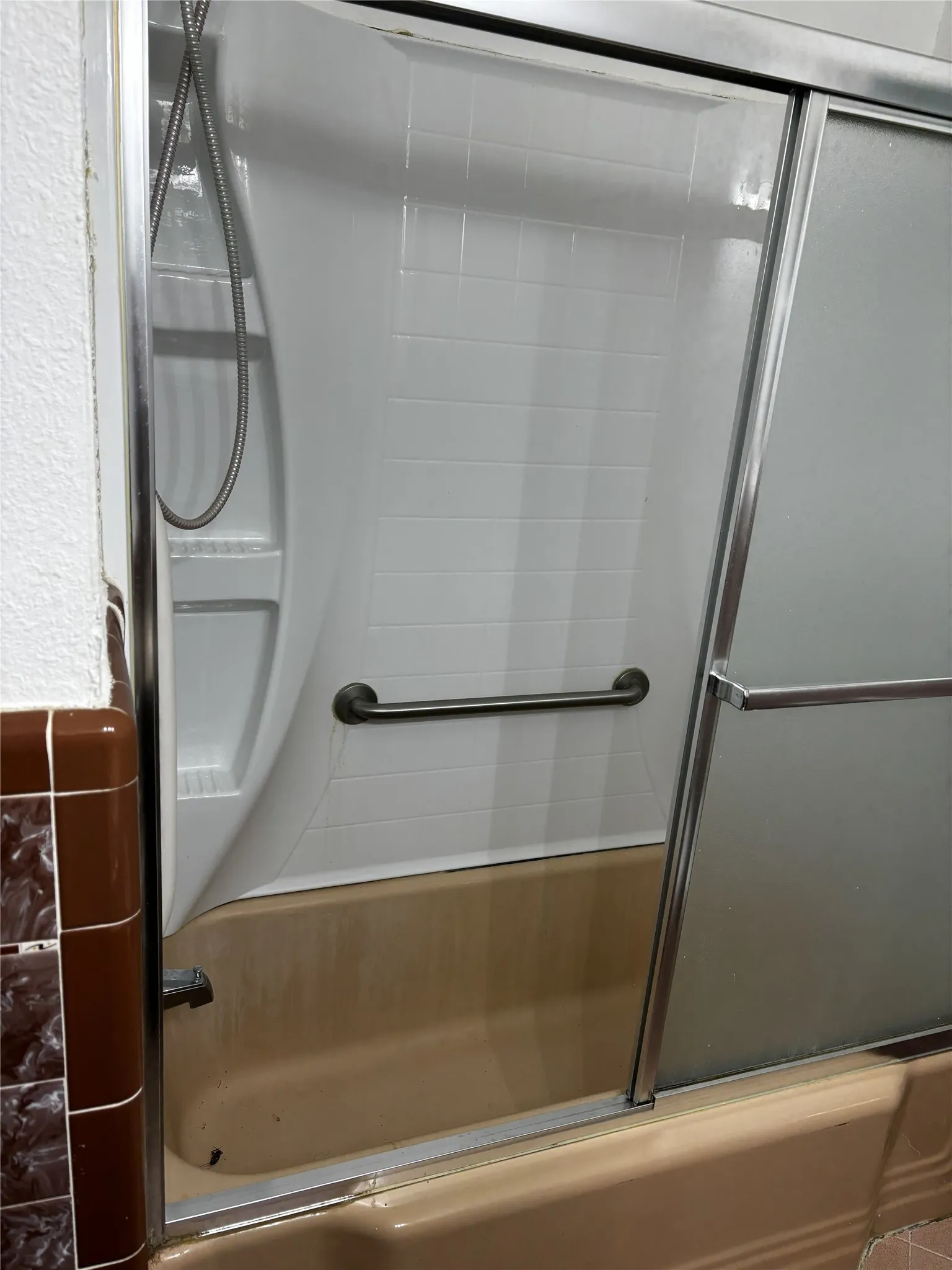 Bathtub with a sliding glass shower enclosure, integrated grab bar, and white subway tile-patterned shower surround