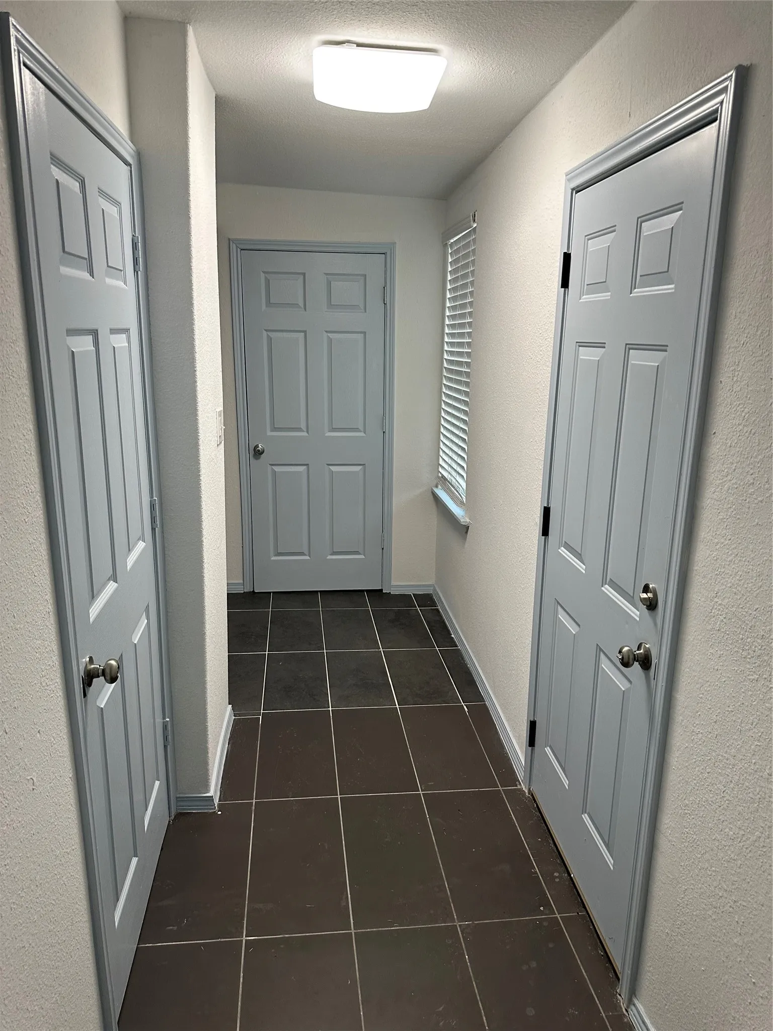 Hallway featuring dark square tile flooring, light-colored walls, and multiple paneled doors