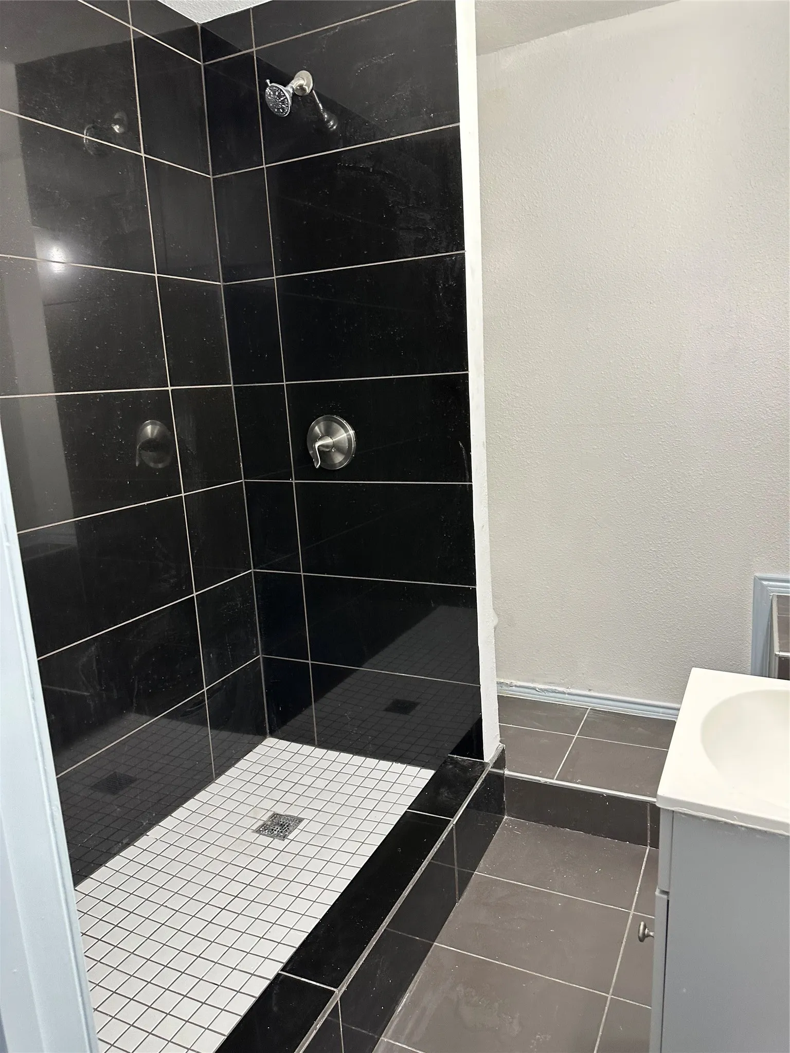 Shower with black tile surround and white mosaic tile flooring
