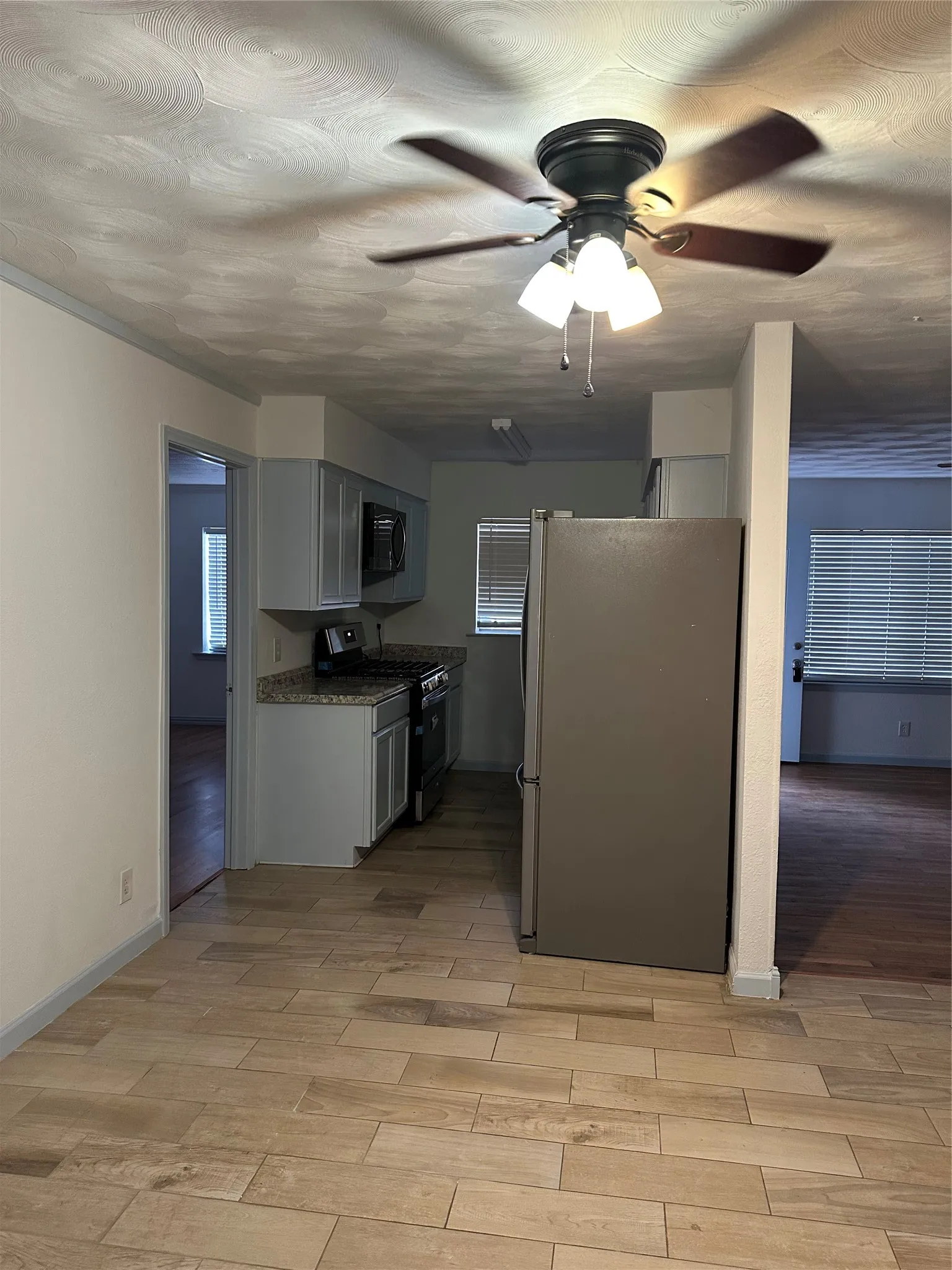 Kitchen featuring wood-finish tile flooring, light gray cabinetry, stainless steel refrigerator, and granite-style countertops