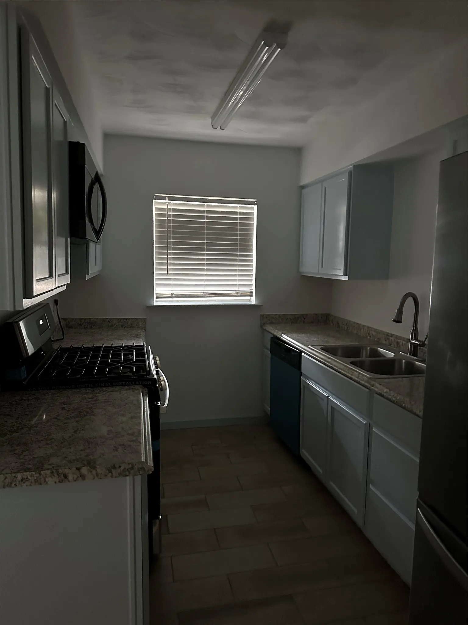 Kitchen featuring light-toned cabinetry, granite-style countertops, stainless steel sink, black range, and wood-finish flooring