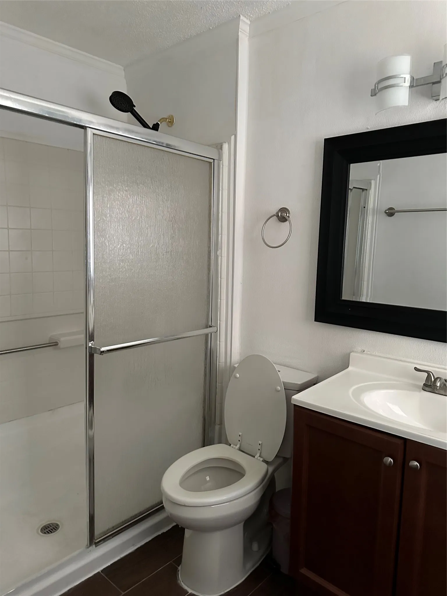 Shower/tub combination with sliding glass doors, dark wood-finish vanity with white countertop and integrated sink, wall-mounted lighting, and dark-framed mirror