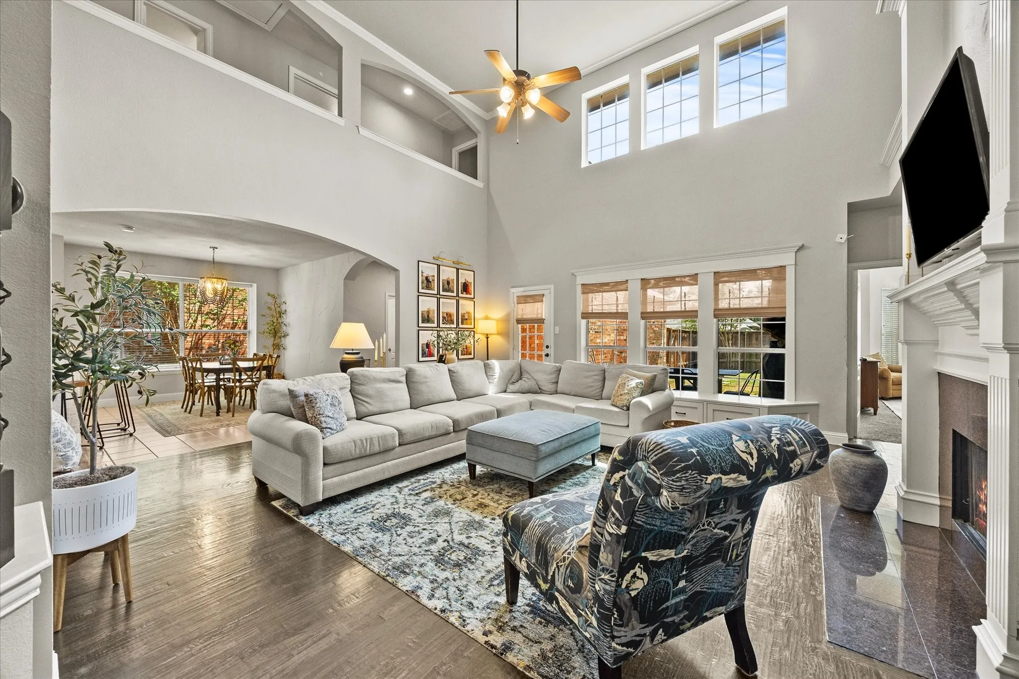 1602 Mapleleaf Drive Wylie, TX 75098 Vaulted ceilings with an upper architectural archway, dark wood-finish flooring, a built-in fireplace with a white mantel, and a multi-pane window array