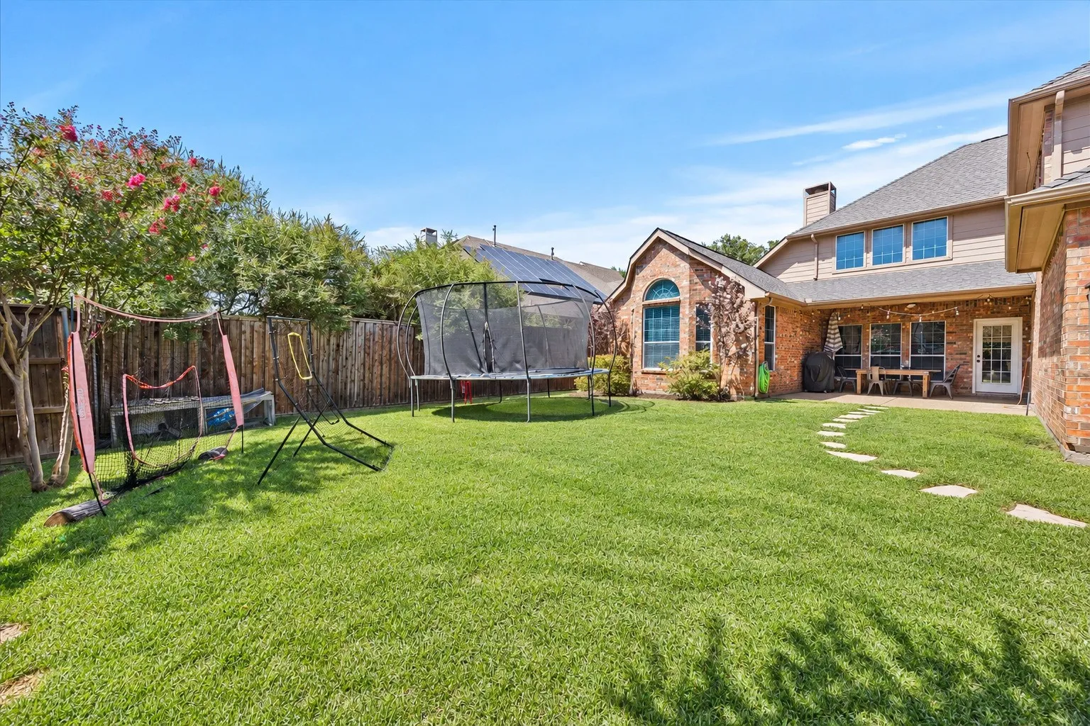 Expansive lawn, brick exterior, covered patio, arched window, and mature perimeter trees
