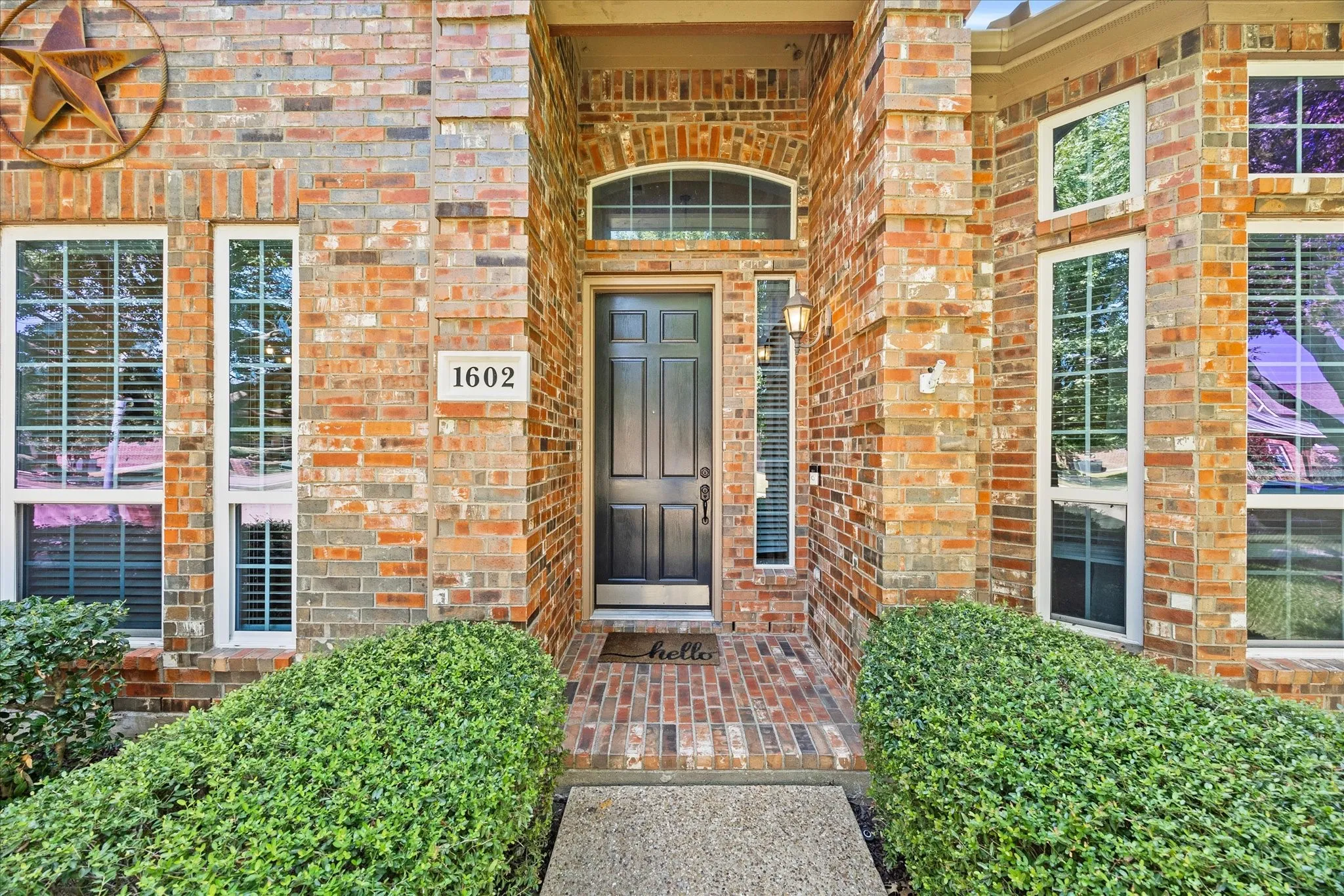 1602 Mapleleaf Drive Wylie, TX 75098 Brick facade with multiple window configurations, arched entryway detail, dark paneled front door, and a concrete walkway