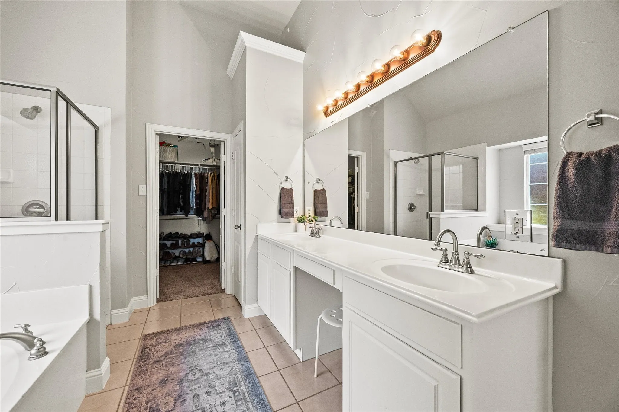 Bathroom featuring a dual vanity with integrated sinks, a built-in makeup counter, a large frameless mirror, and tiled flooring