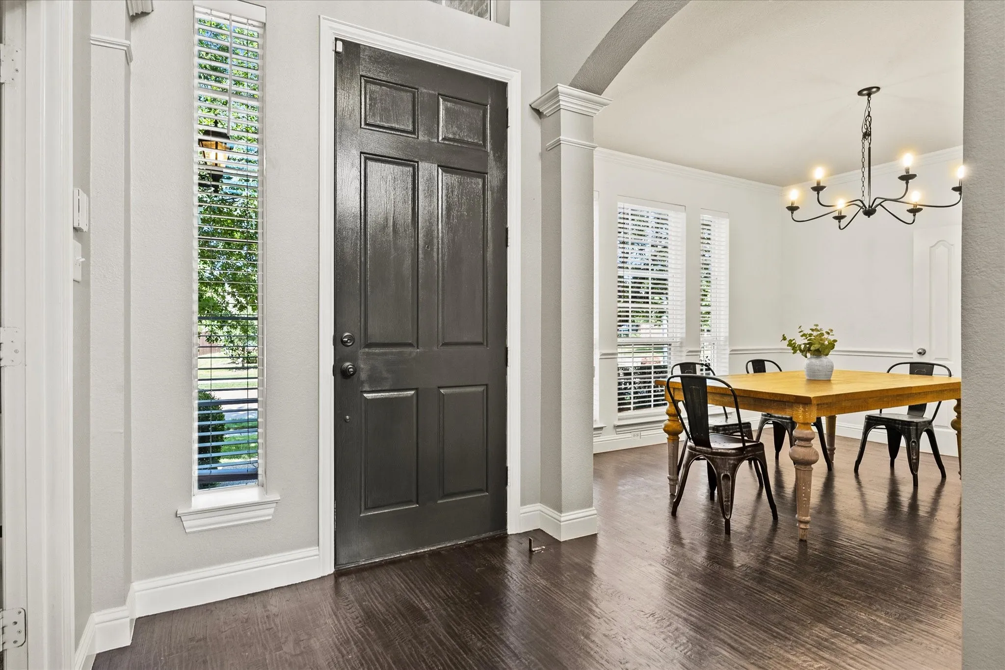 1602 Mapleleaf Drive Wylie, TX 75098 Dark wood-finish flooring, paneled entry door, vertical window with blinds, architectural archway with pillars, and an overhead chandelier