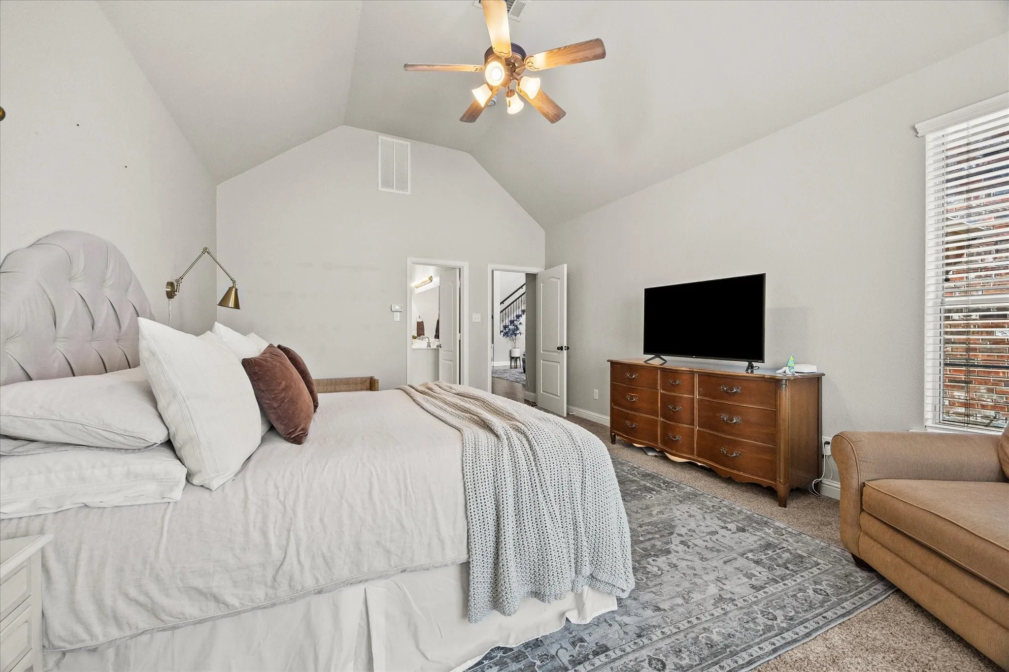 Vaulted ceiling with a ceiling fan, wall-mounted sconce lighting, and wood-finish flooring