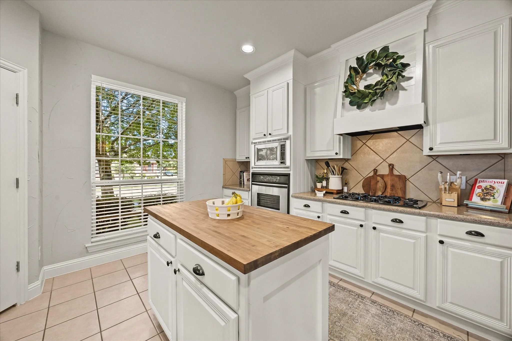 1602 Mapleleaf Drive Wylie, TX 75098 White cabinetry with black hardware, wood-finish island countertop, tile flooring, built-in stainless steel appliances, and a tiled backsplash