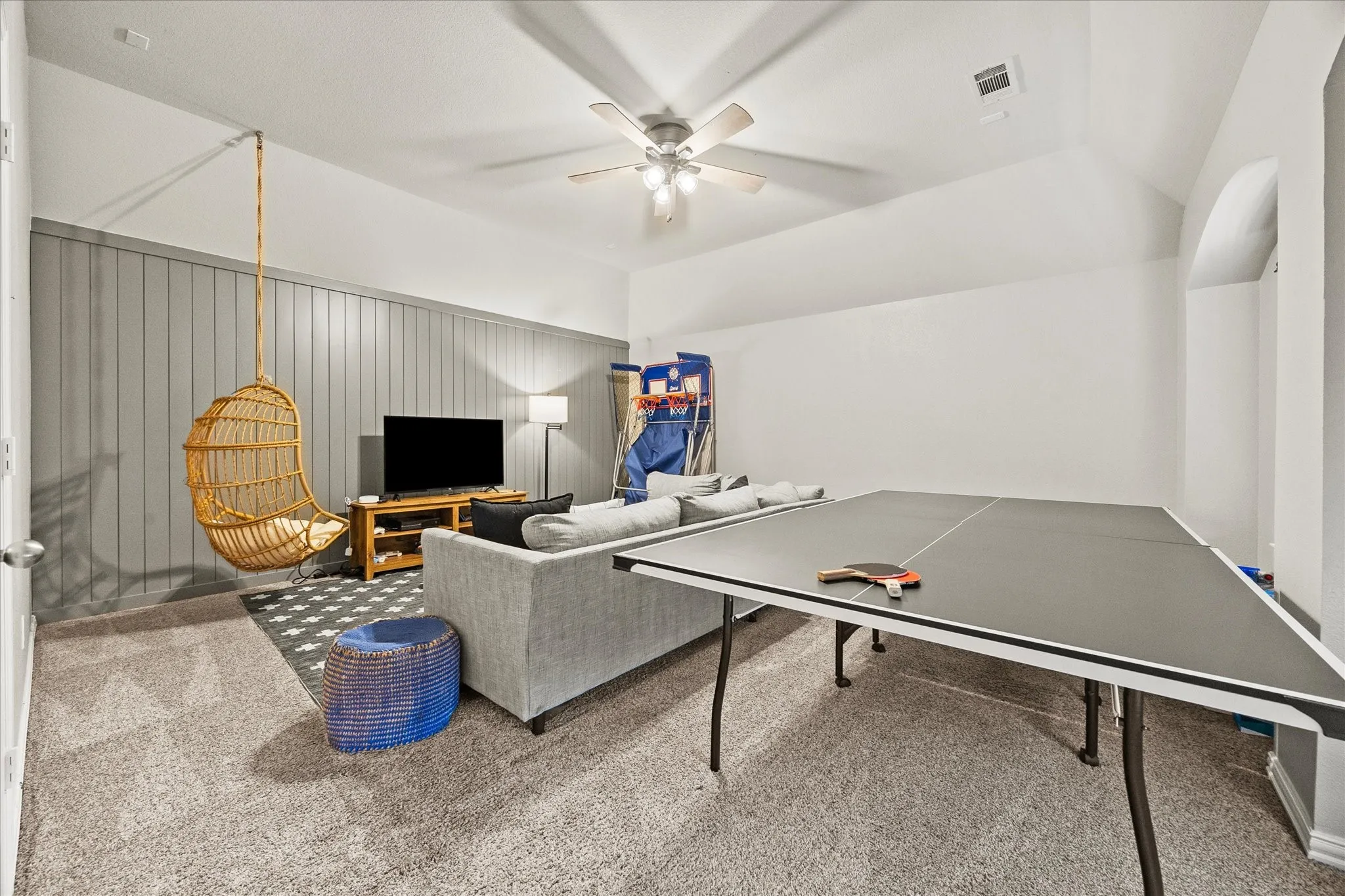 Vaulted ceiling with a ceiling fan, accent wall with vertical paneling, and carpet flooring