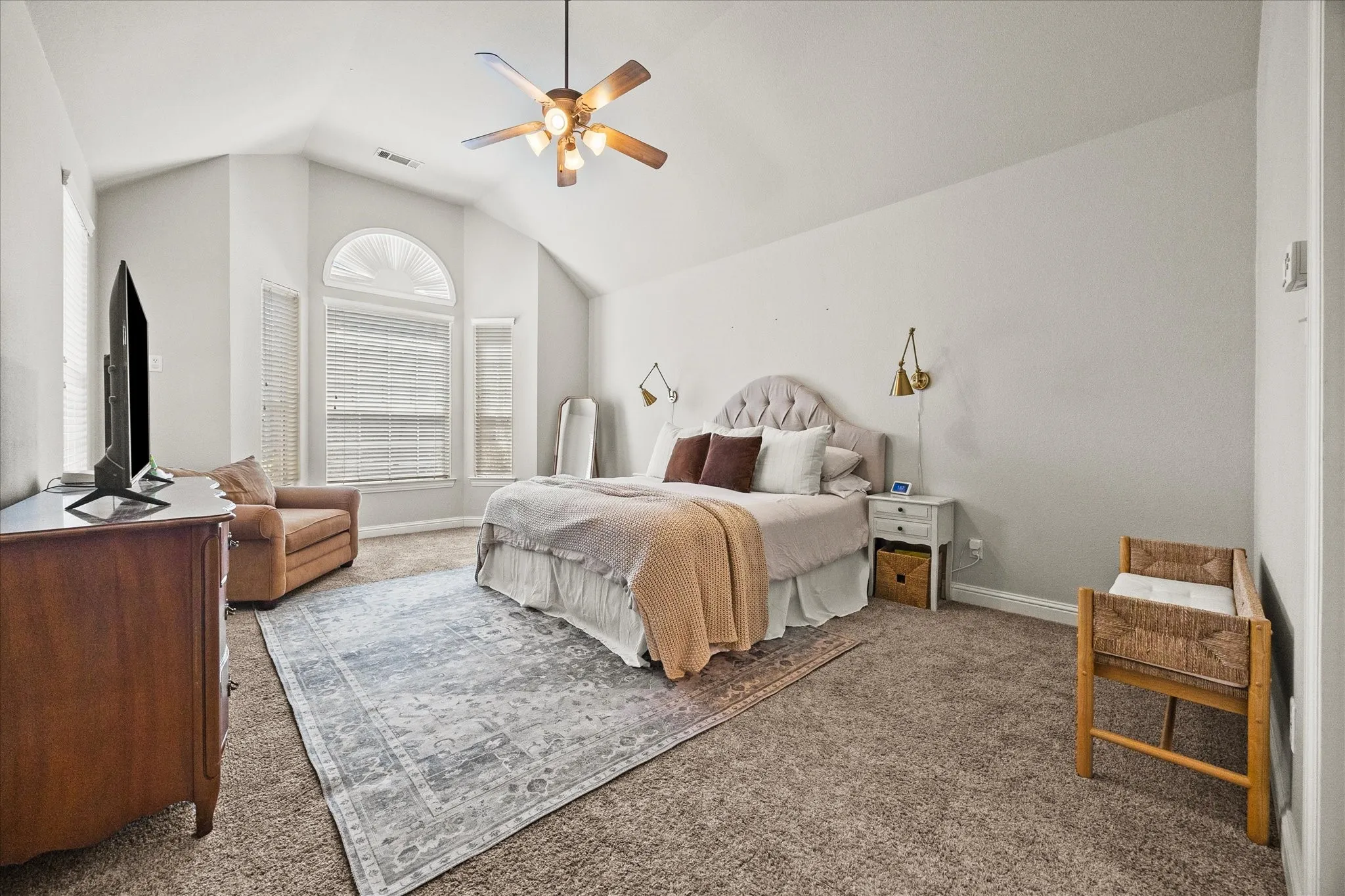Vaulted ceiling with a ceiling fan, arched window, multiple windows with blinds, and neutral carpeting