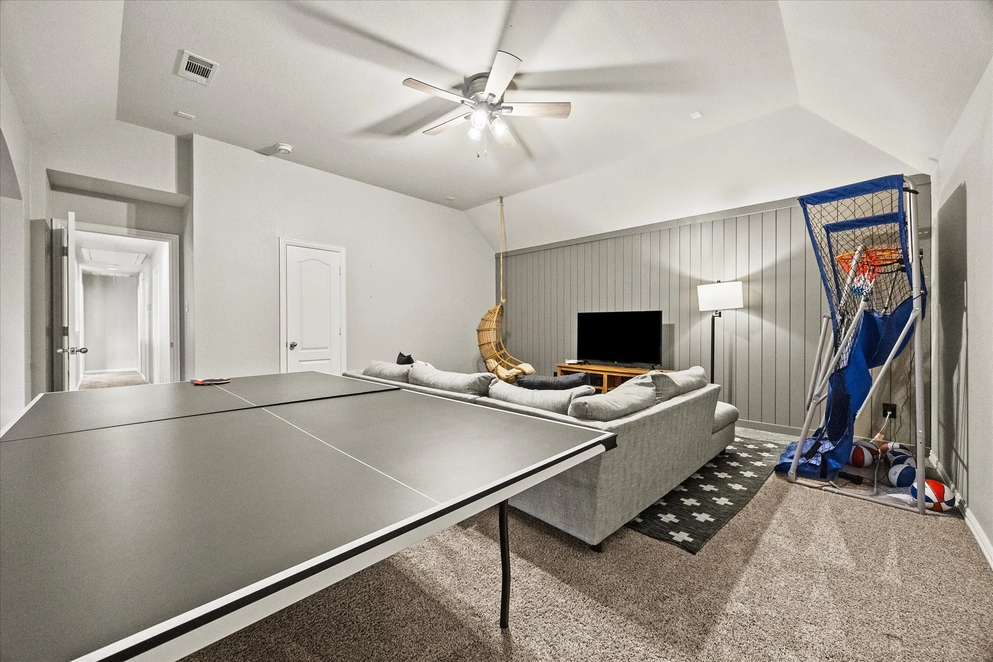 Spacious room with sloped ceilings, ceiling fan, and paneled accent wall