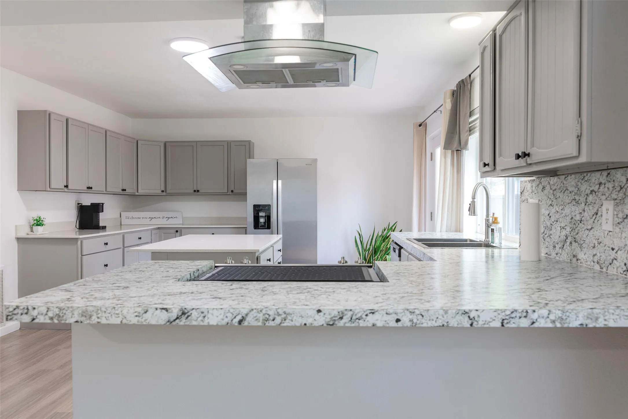 Sleek kitchen featuring gray cabinetry, stainless steel appliances, speckled countertops, a built-in cooktop, and a glass-accented range hood