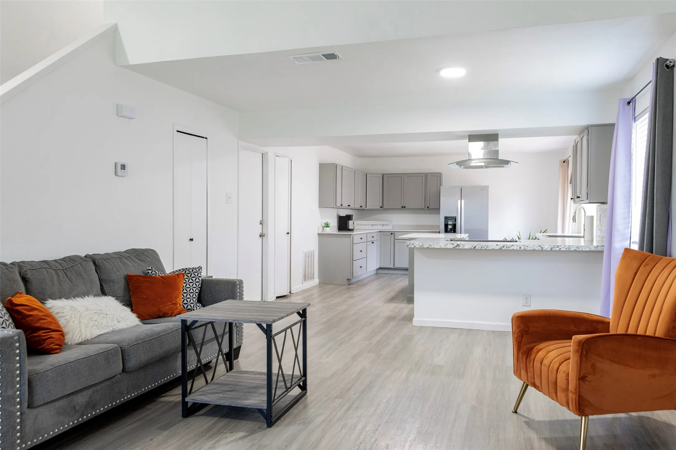 Open-concept living space featuring wood-finish flooring, recessed lighting, and a kitchen with gray cabinetry, stainless steel appliances, and a central island with a light-toned countertop