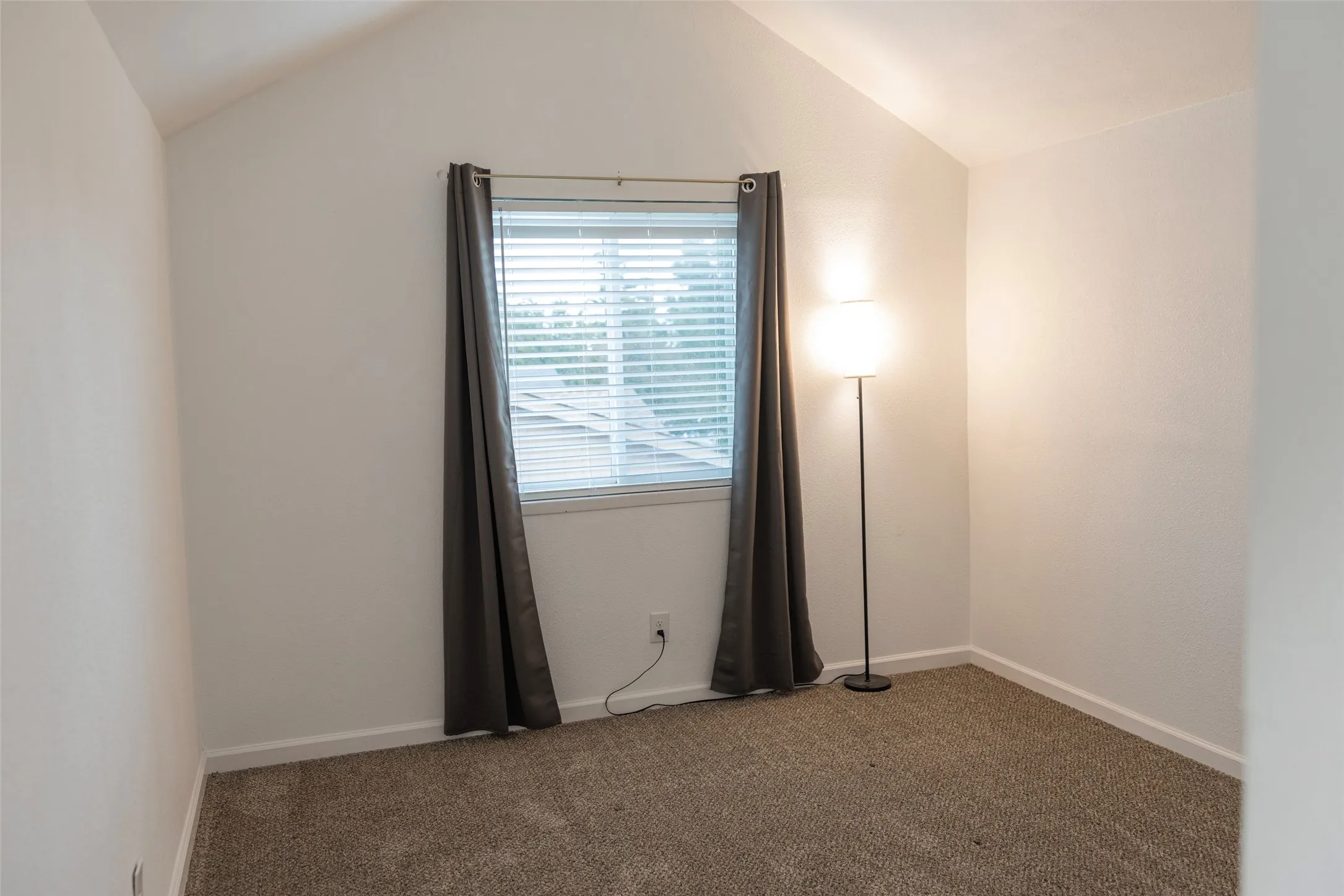Vaulted ceiling, neutral wall tones, carpet flooring, window with blinds