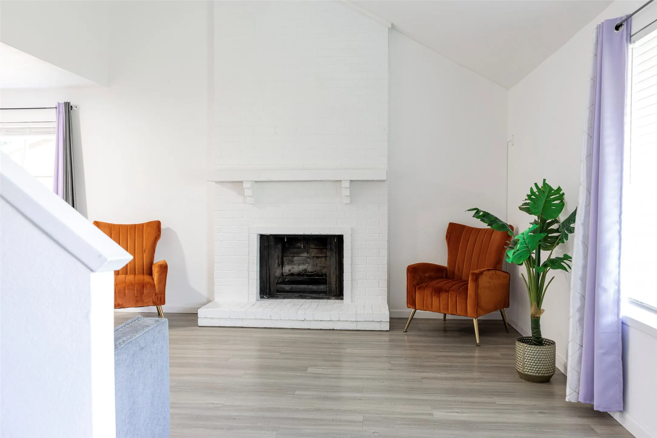 Vaulted ceiling, white painted brick fireplace with mantel, wood-finish flooring, and white walls