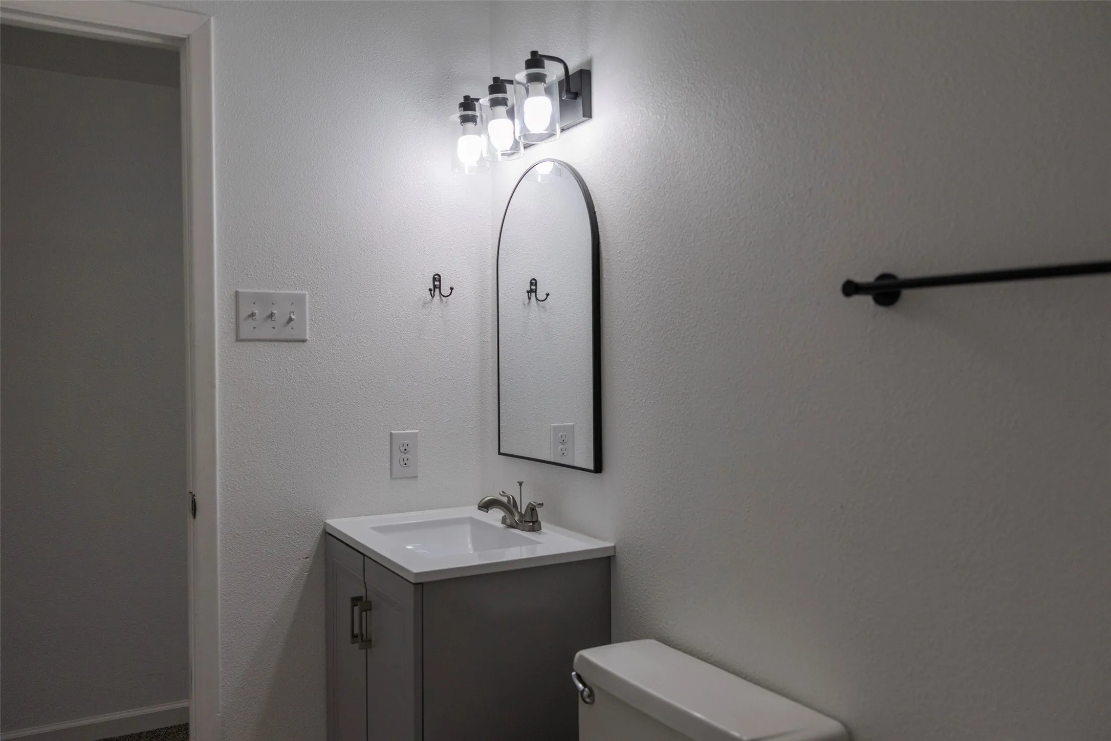 Vanity with integrated sink, modern arched mirror, and multi-bulb vanity light fixture