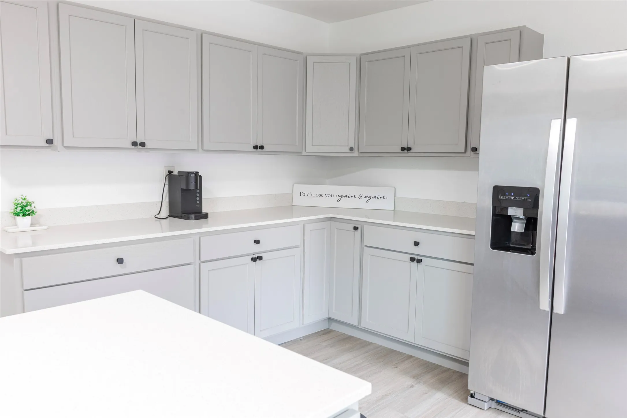 Light gray cabinetry, white countertops, wood-finish flooring, and a stainless steel side-by-side refrigerator