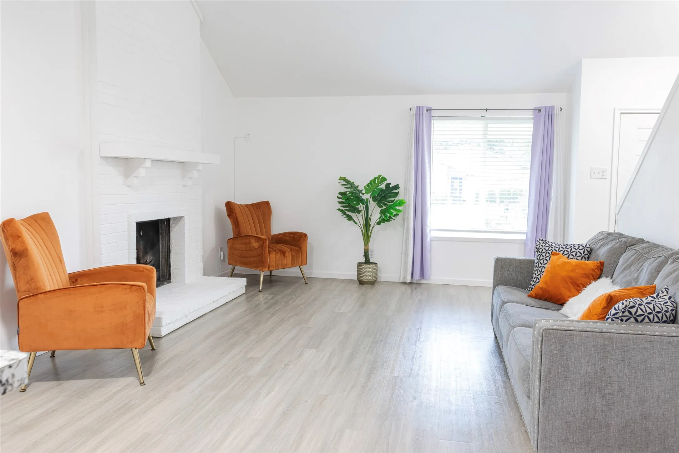 Living area featuring a white brick fireplace with a mantel, light wood-finish flooring, and a large window