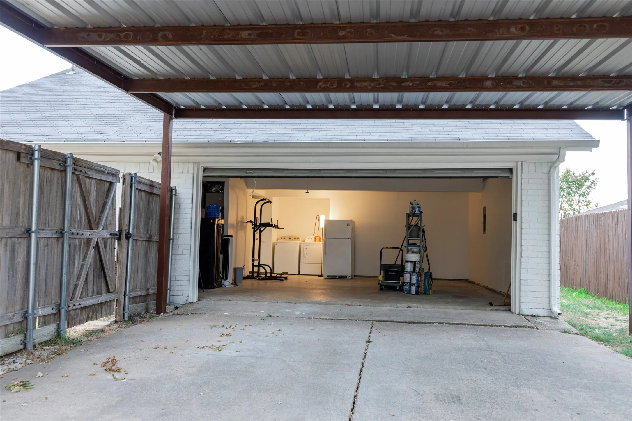 Carport with metal roofing, concrete driveway, white brick exterior, and a wooden privacy fence