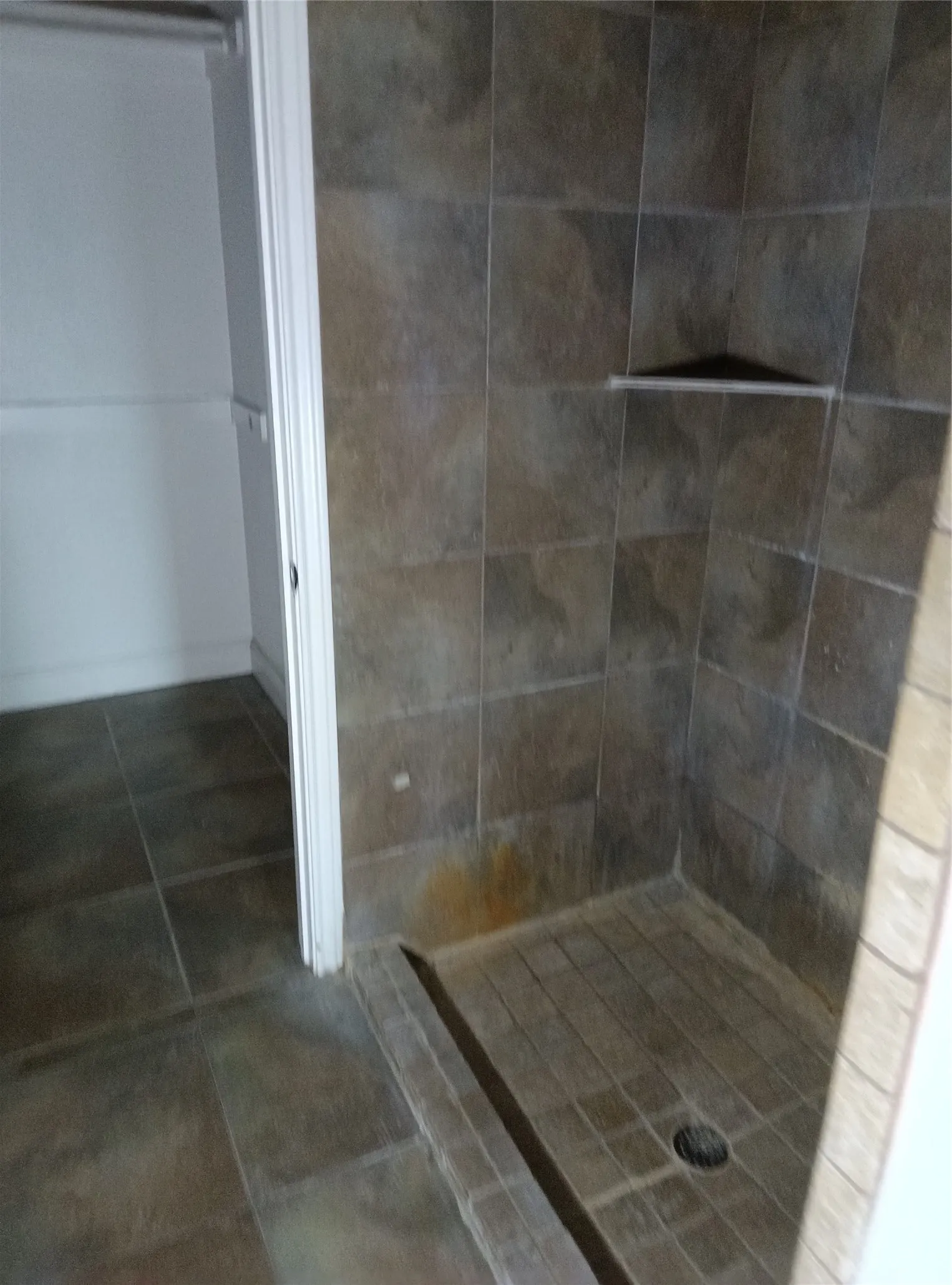 Walk-in shower with tiled walls and floor, complete with a corner shelf